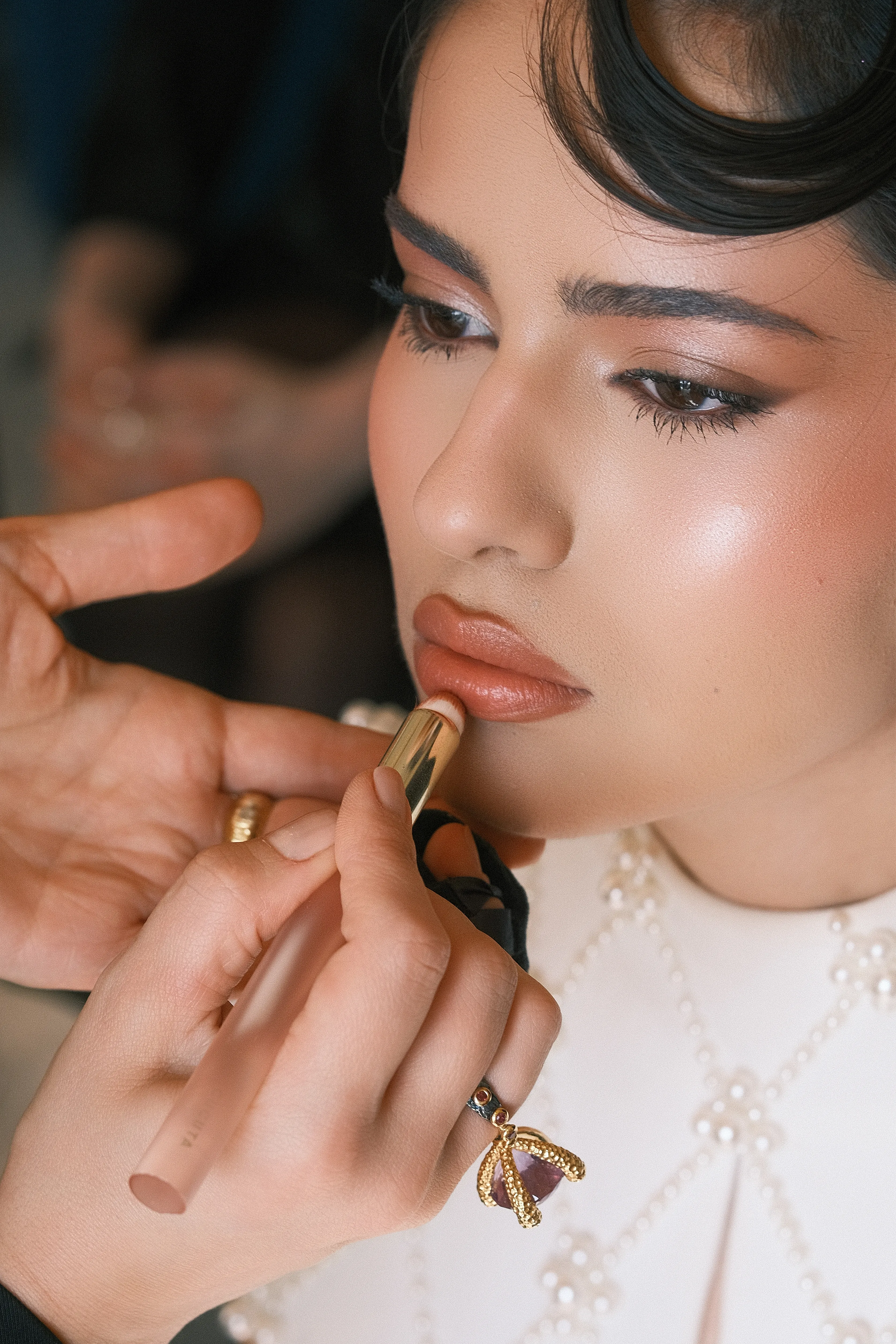 Macro shot of lipstick application with a gold ring visible on the hand