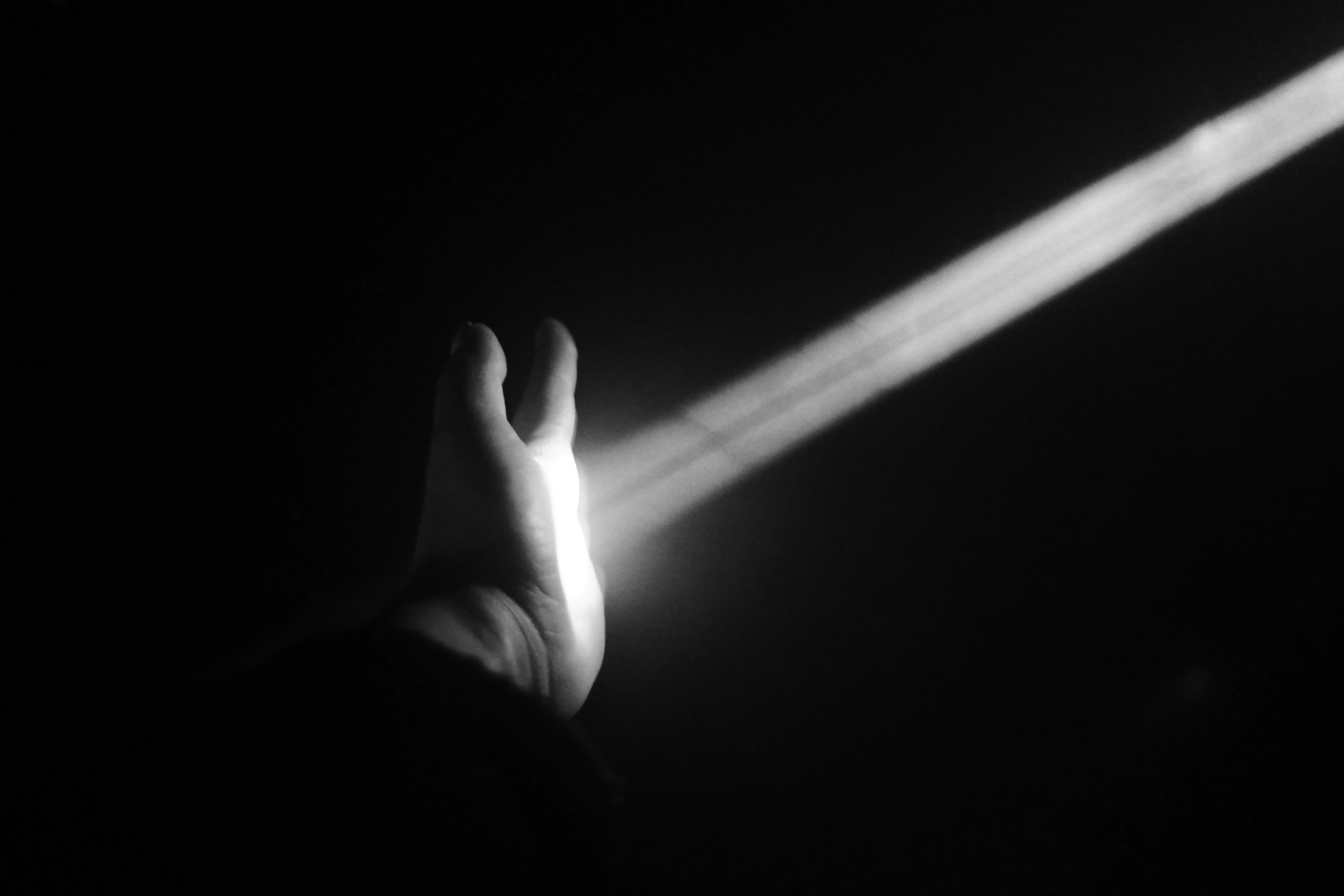 A single beam of light crossing an open hand in total darkness, in black and white