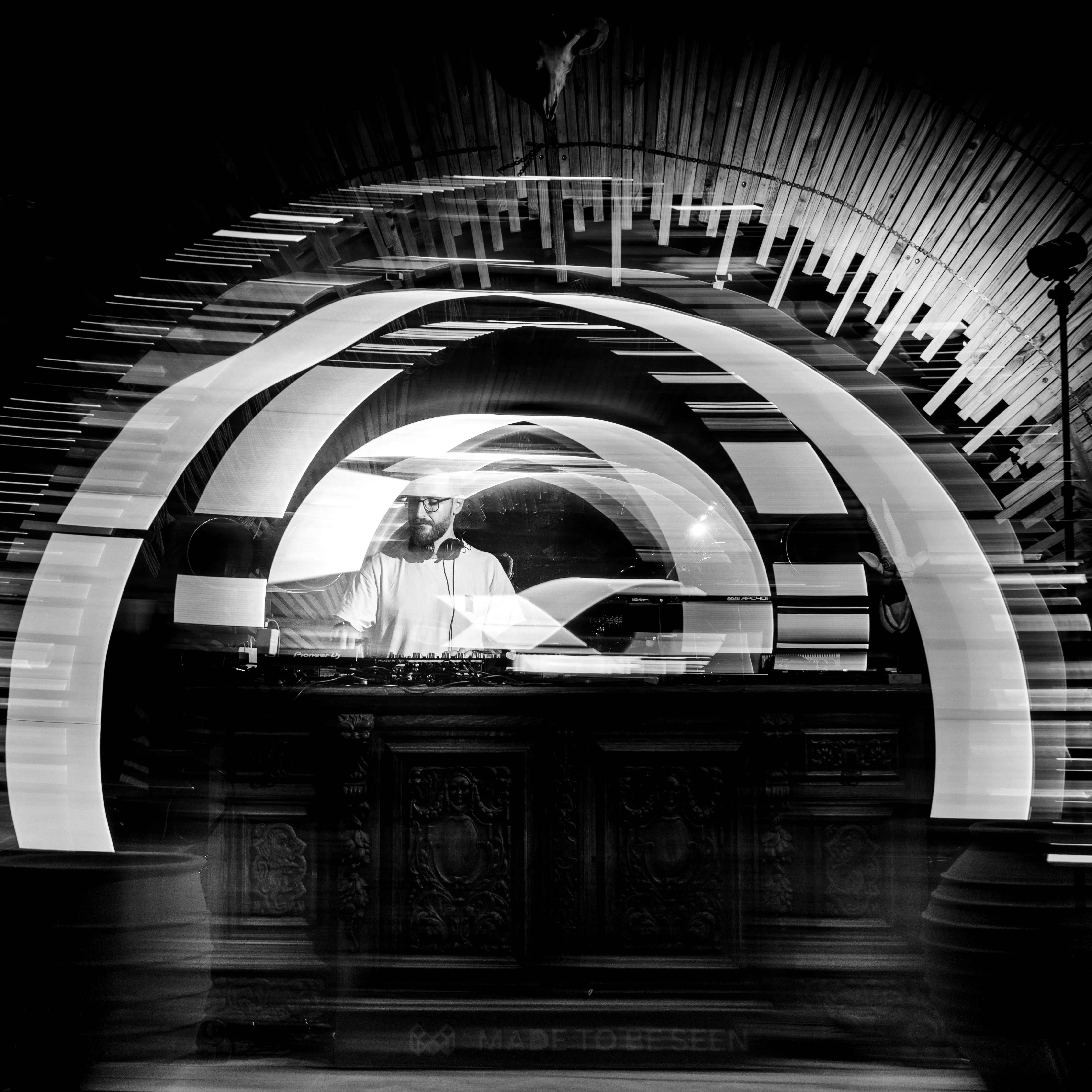 Black and white long exposure of a DJ set, light trails cutting through the dark
