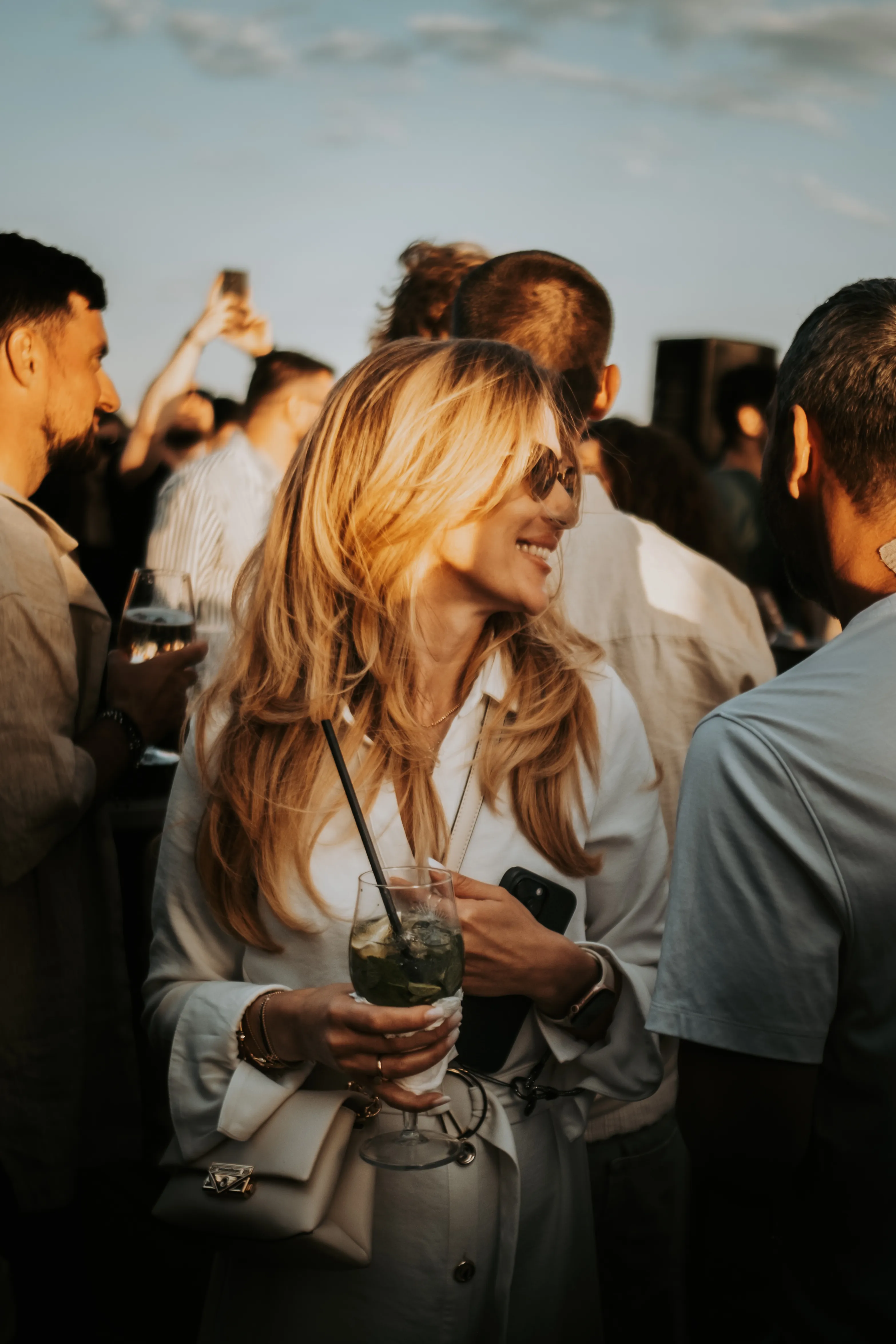 A guest smiling in golden-hour light, holding a mojito, sunlit hair in motion