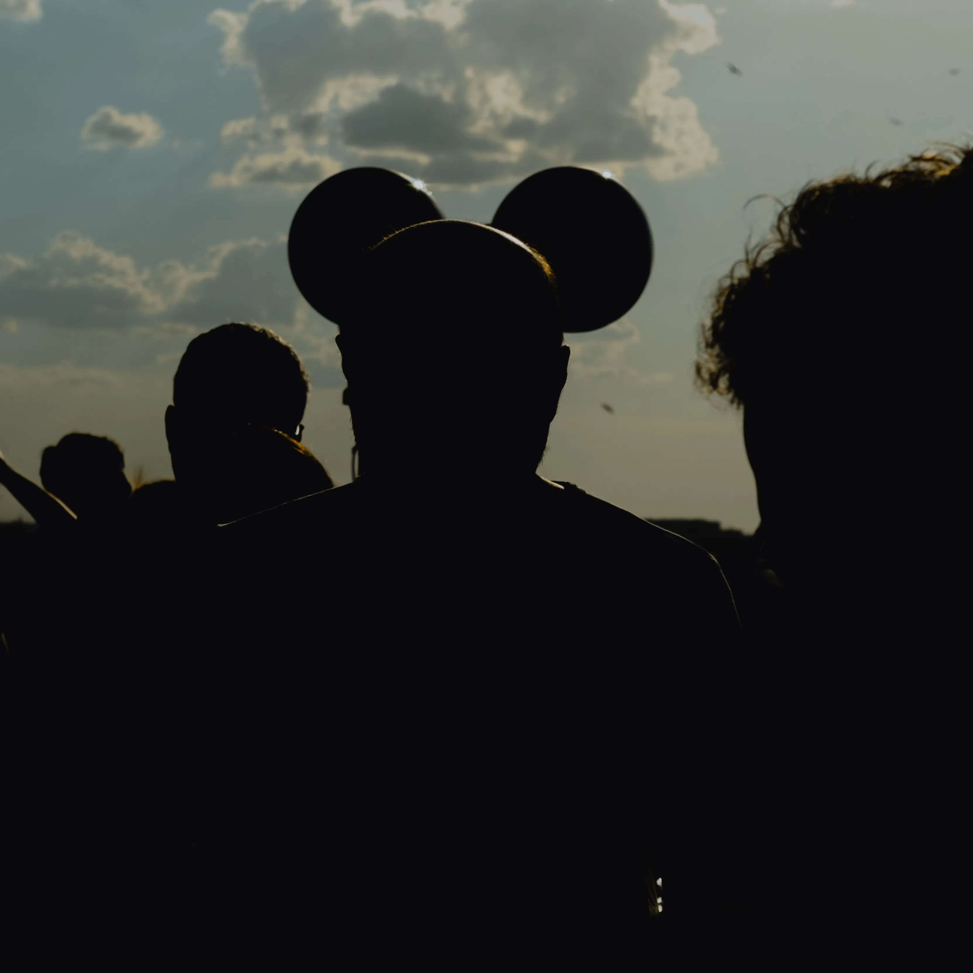 Silhouette of a guest wearing mouse-ear balloons against a dusk sky