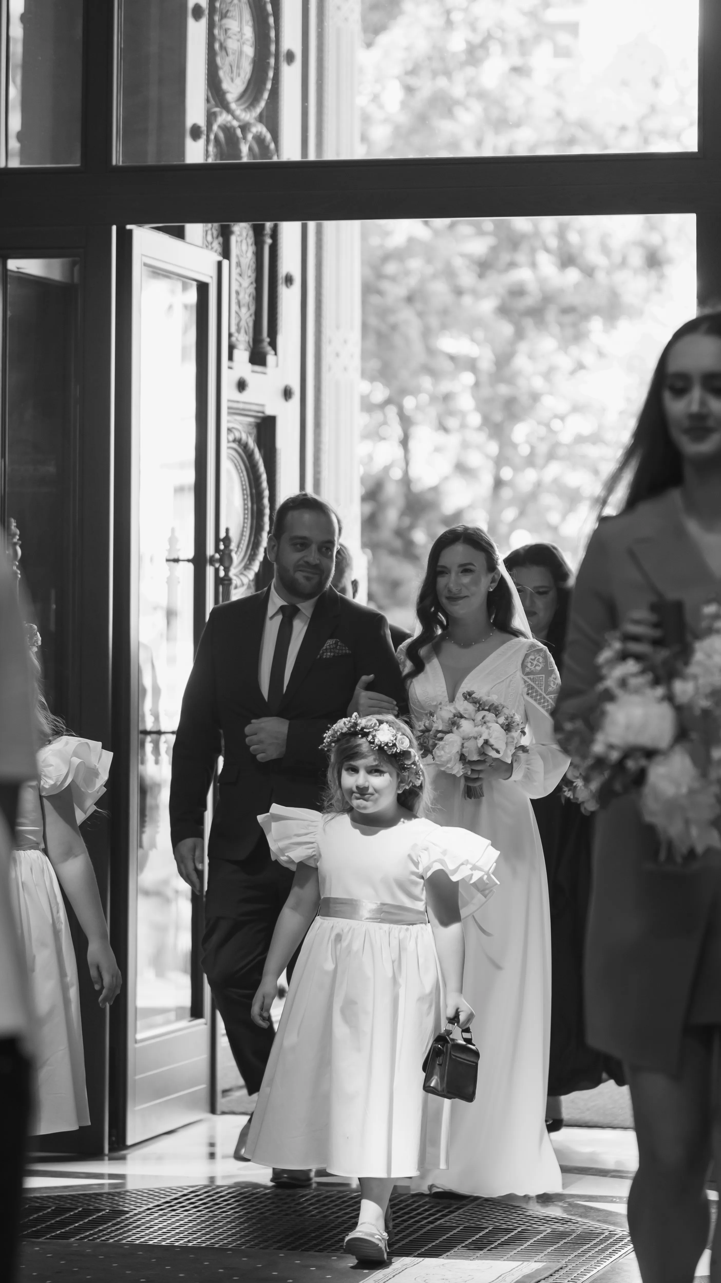 A flower girl and the wedding party entering a doorway, color