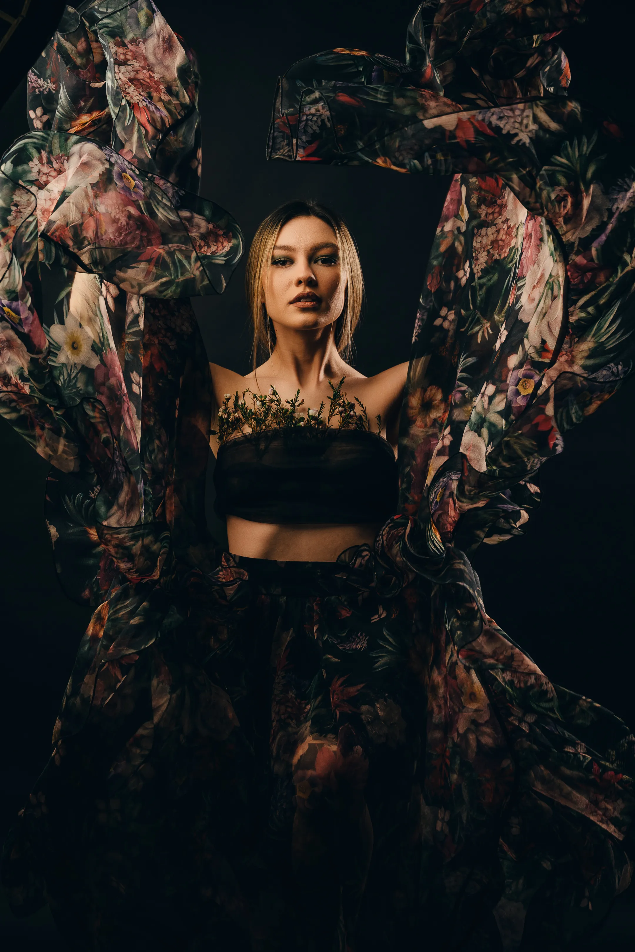 Portrait of a woman framed by billowing floral fabric, dark studio backdrop