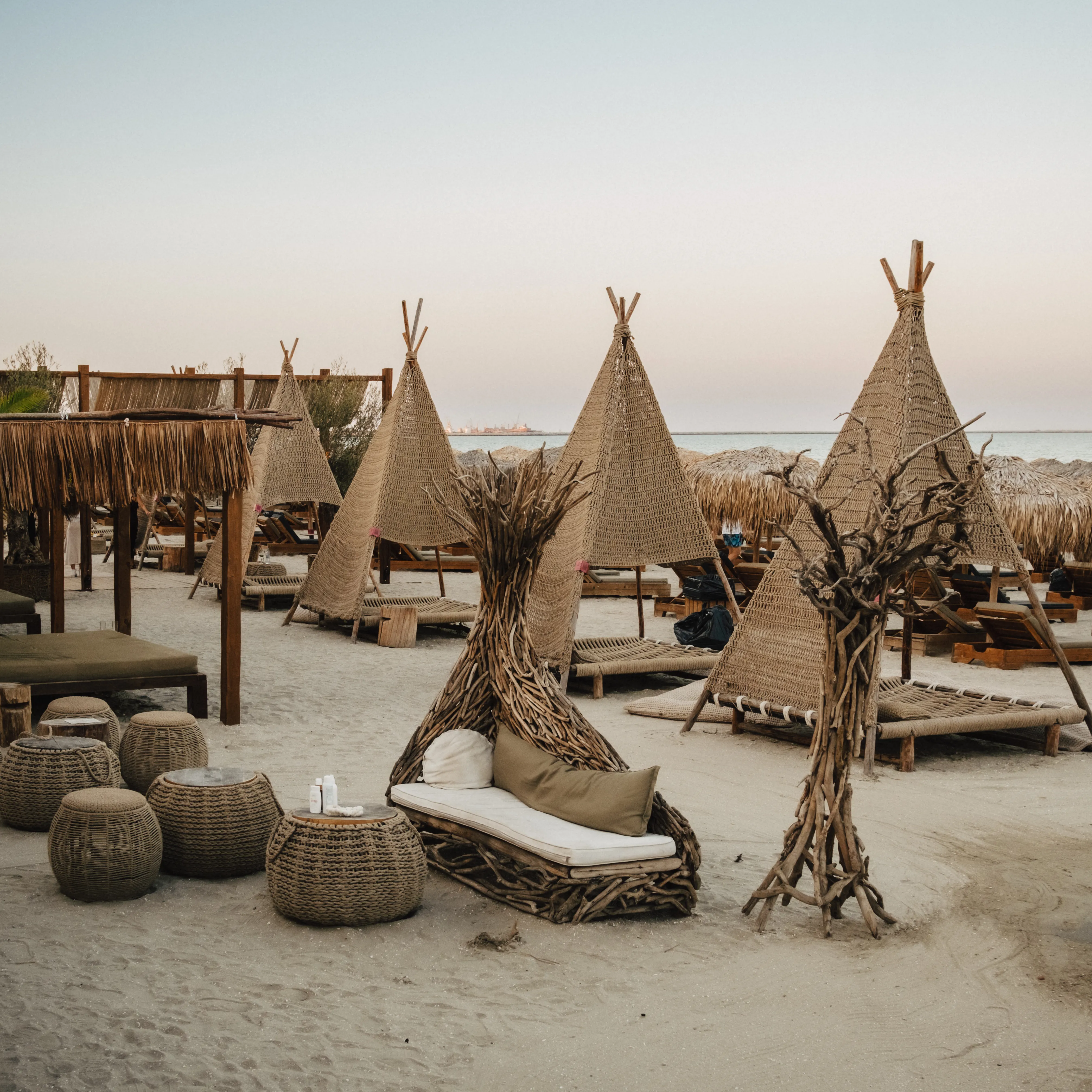 A row of empty thatched daybeds at dusk under a pink sky