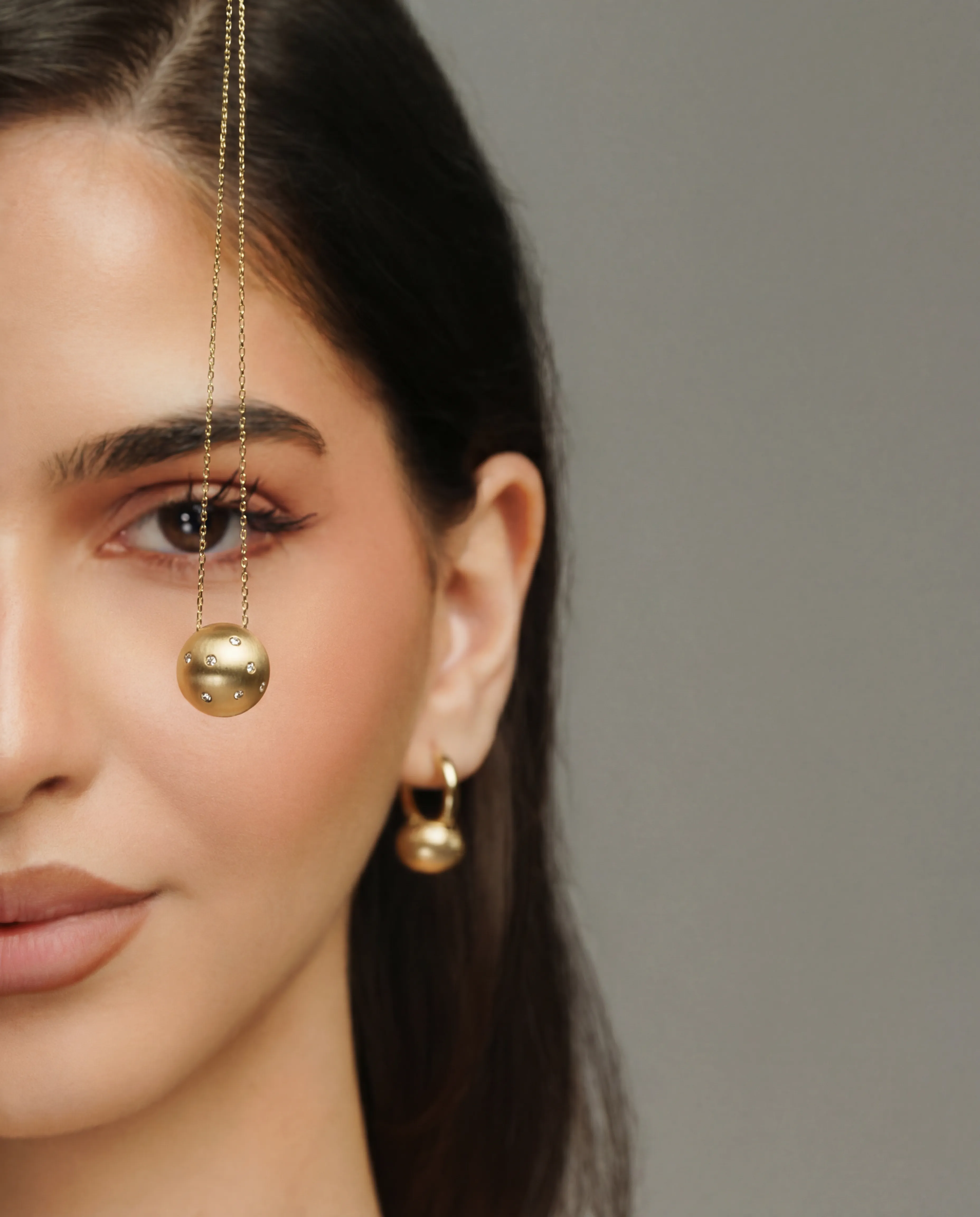 Extreme close-up of half a woman's face, a gold threader earring with a jeweled pendant hanging in front of her eye