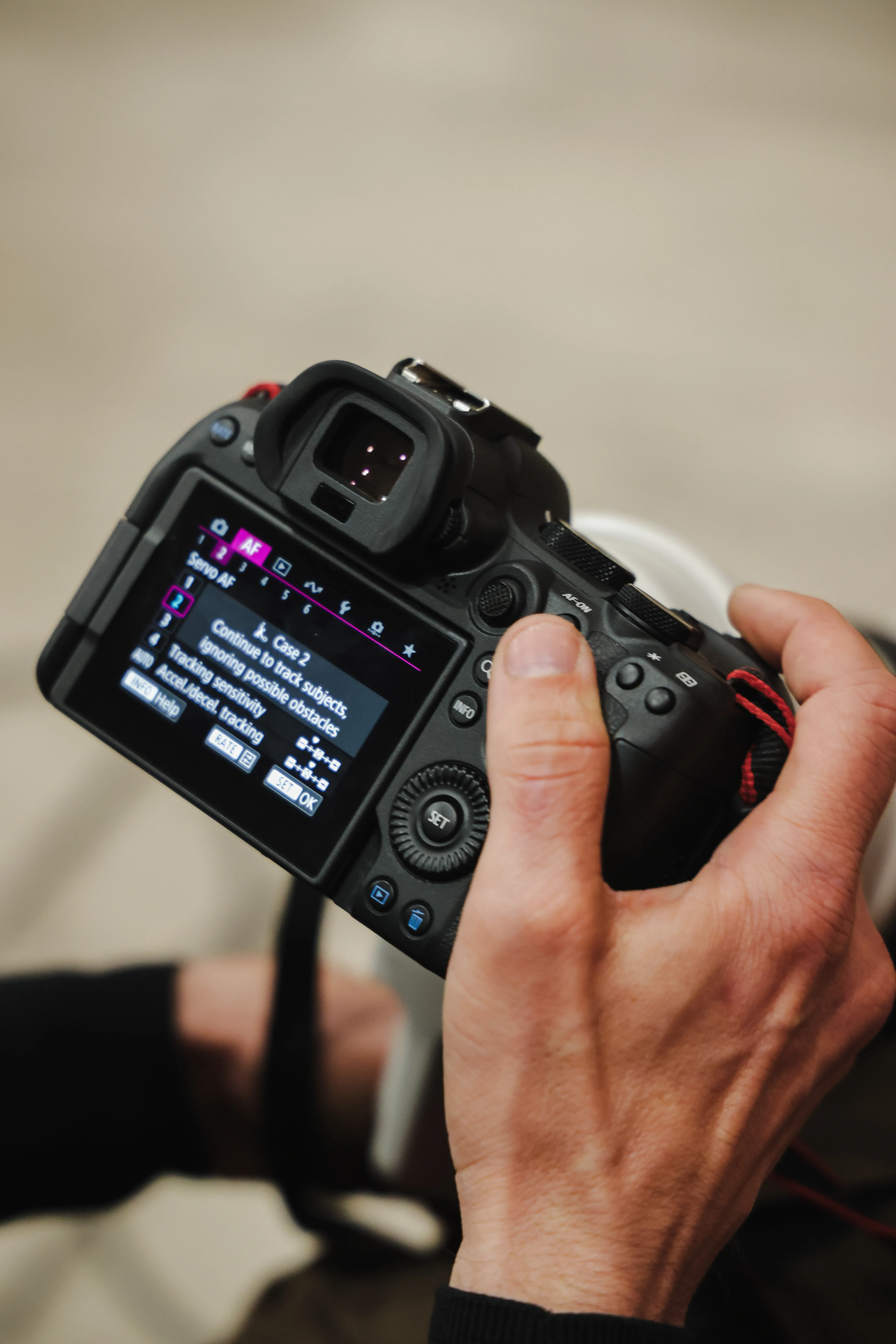 Close-up of a hand holding a Canon EOS R body, reviewing autofocus settings on the rear screen