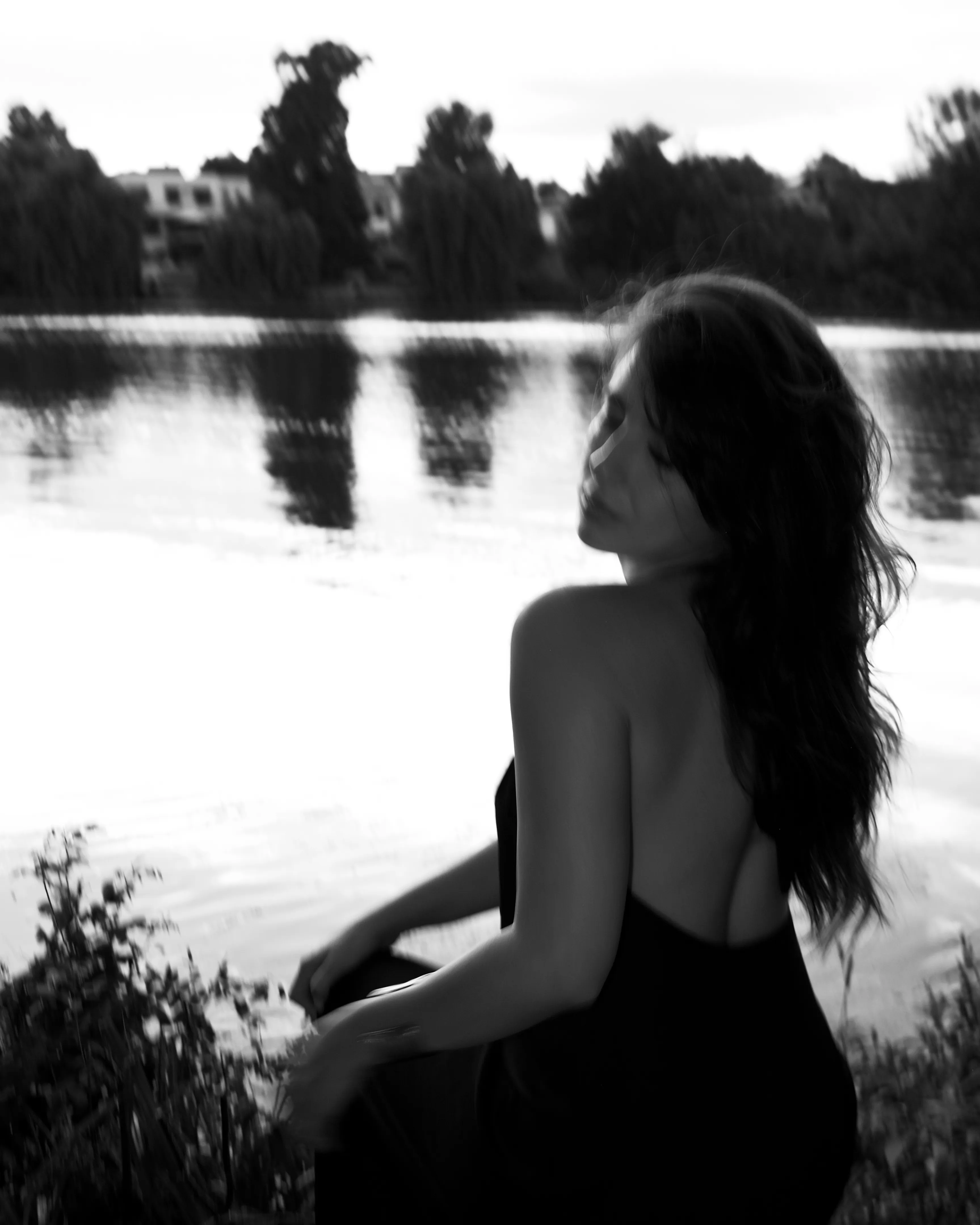 Woman in silhouette by a lake at dusk, wind in her hair, black and white