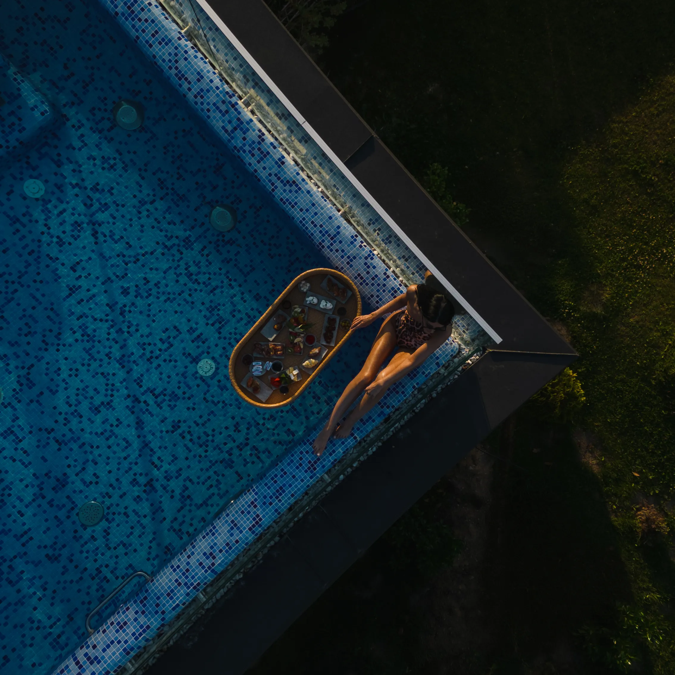 Aerial view of a woman lying on colorful patterned tiles beside a pool
