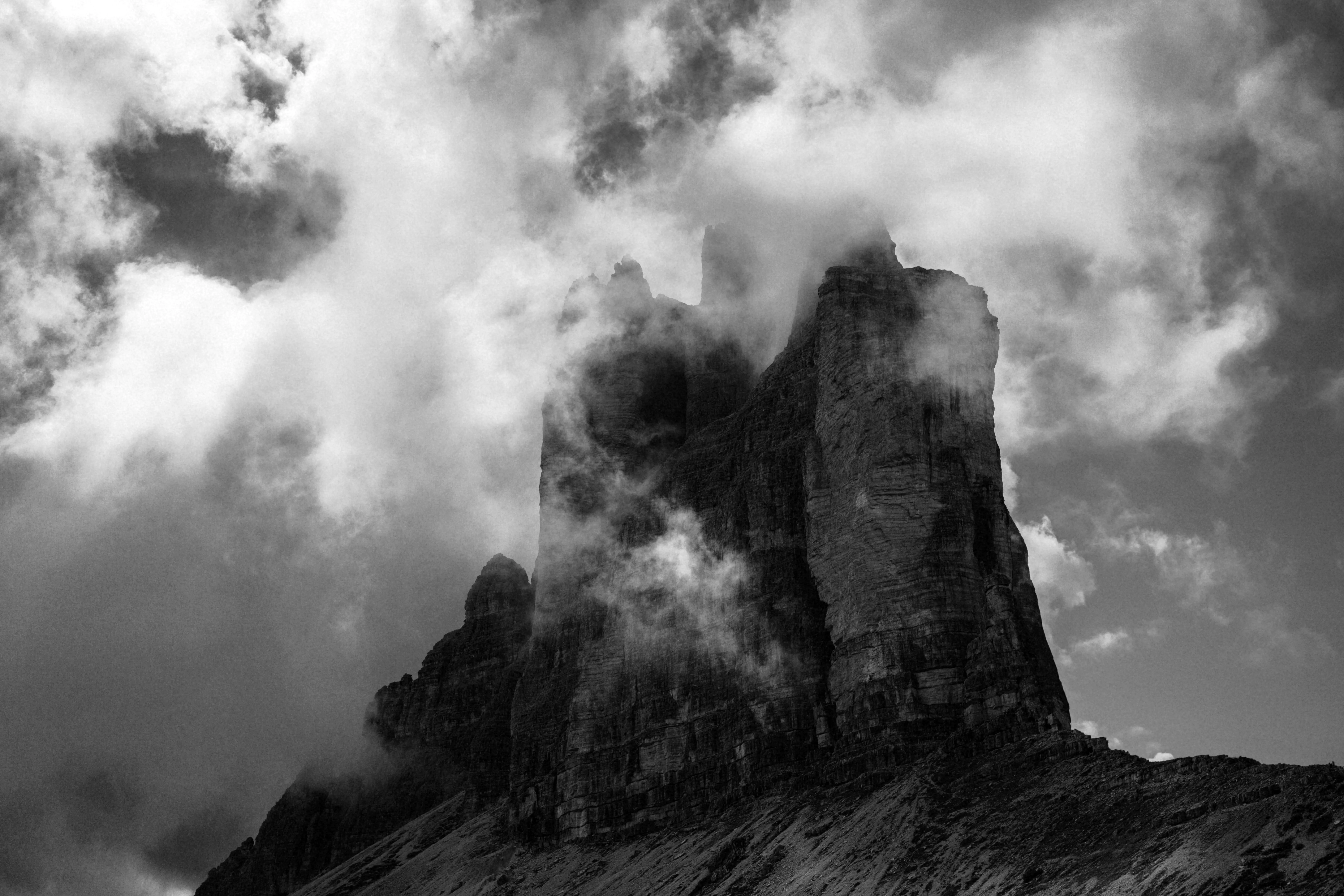 A jagged mountain peak wrapped in storm clouds, in black and white