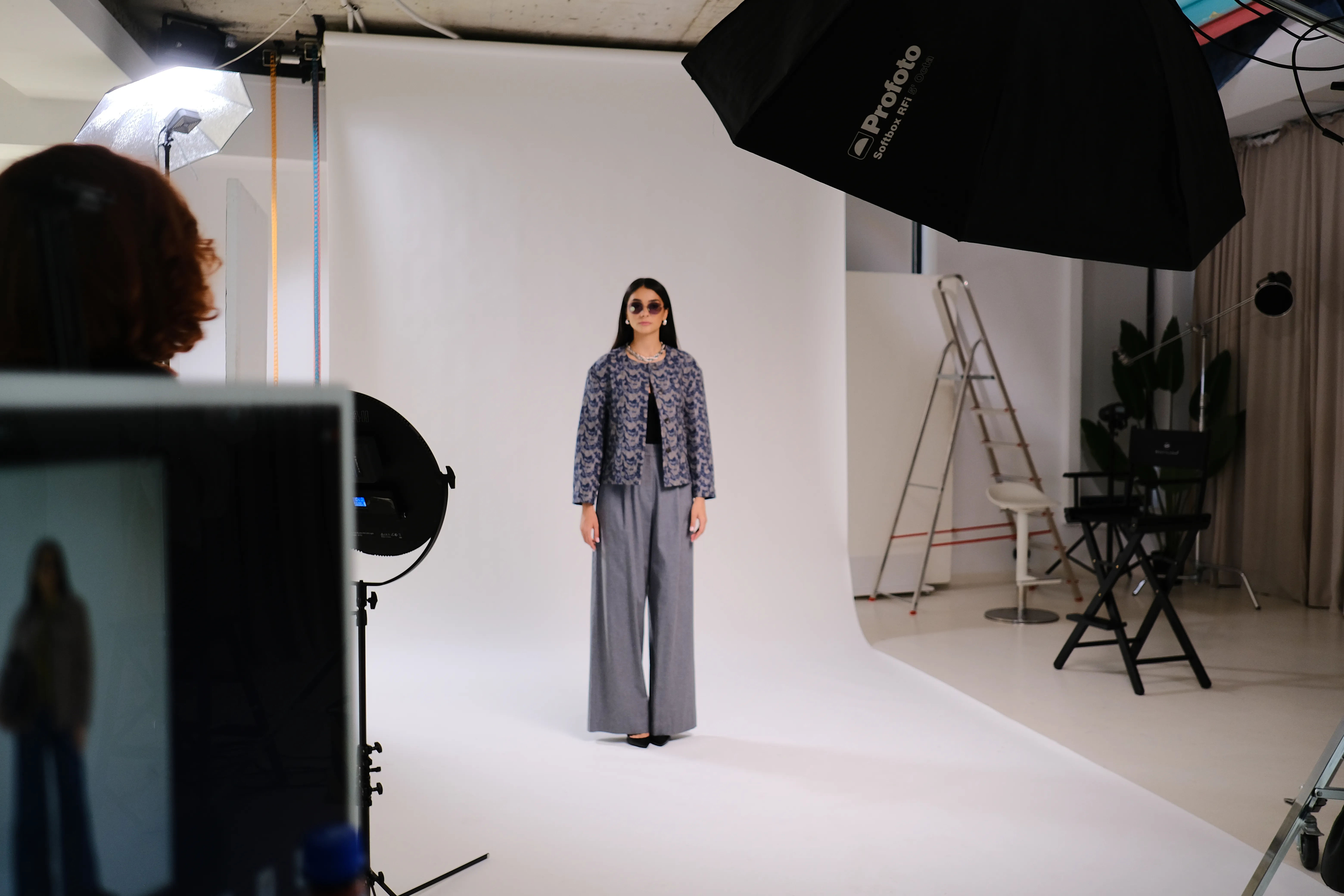 Wide studio view of the shoot in progress, lighting rig and model against a white cyc