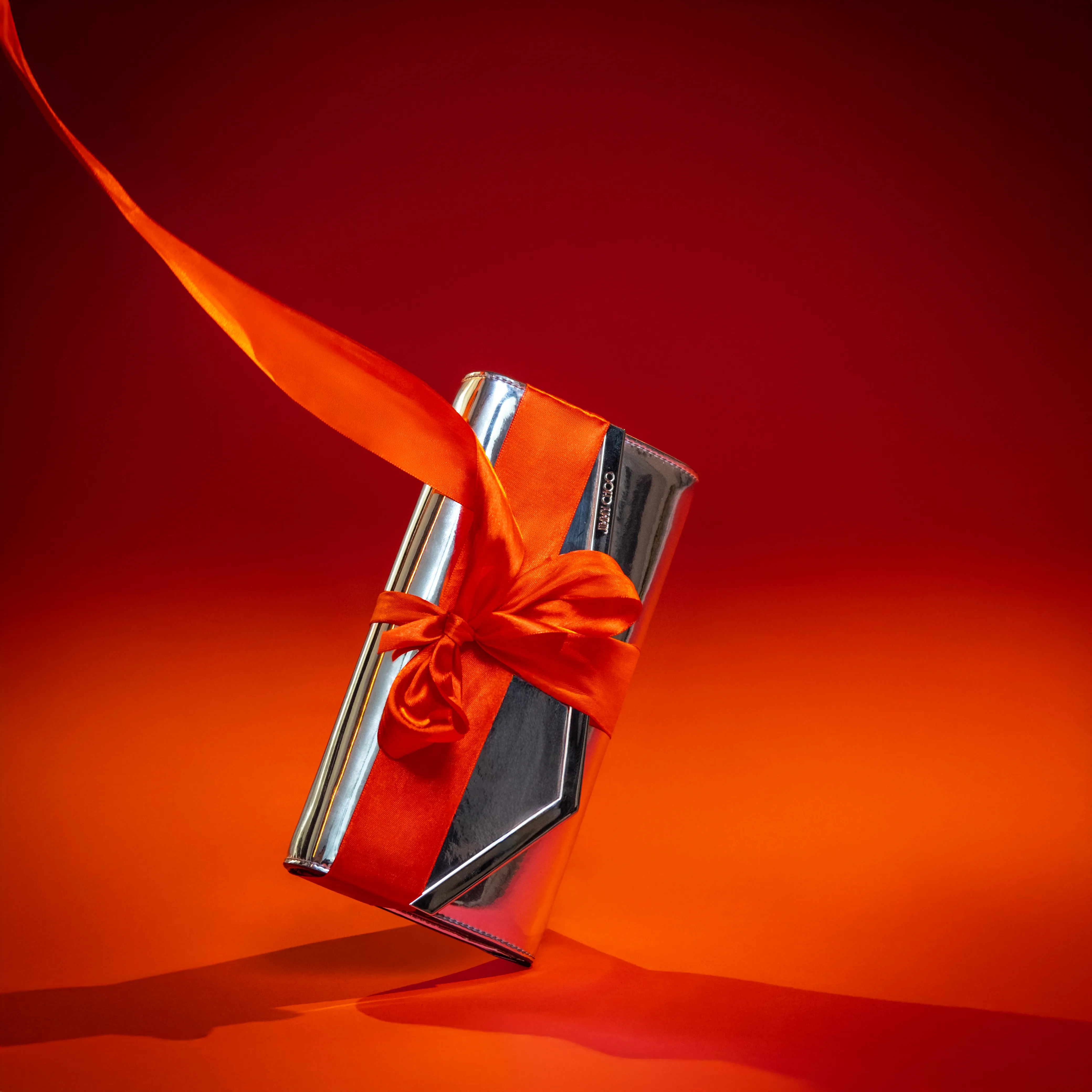 A metallic clutch wrapped with an orange satin ribbon and bow against a red gradient