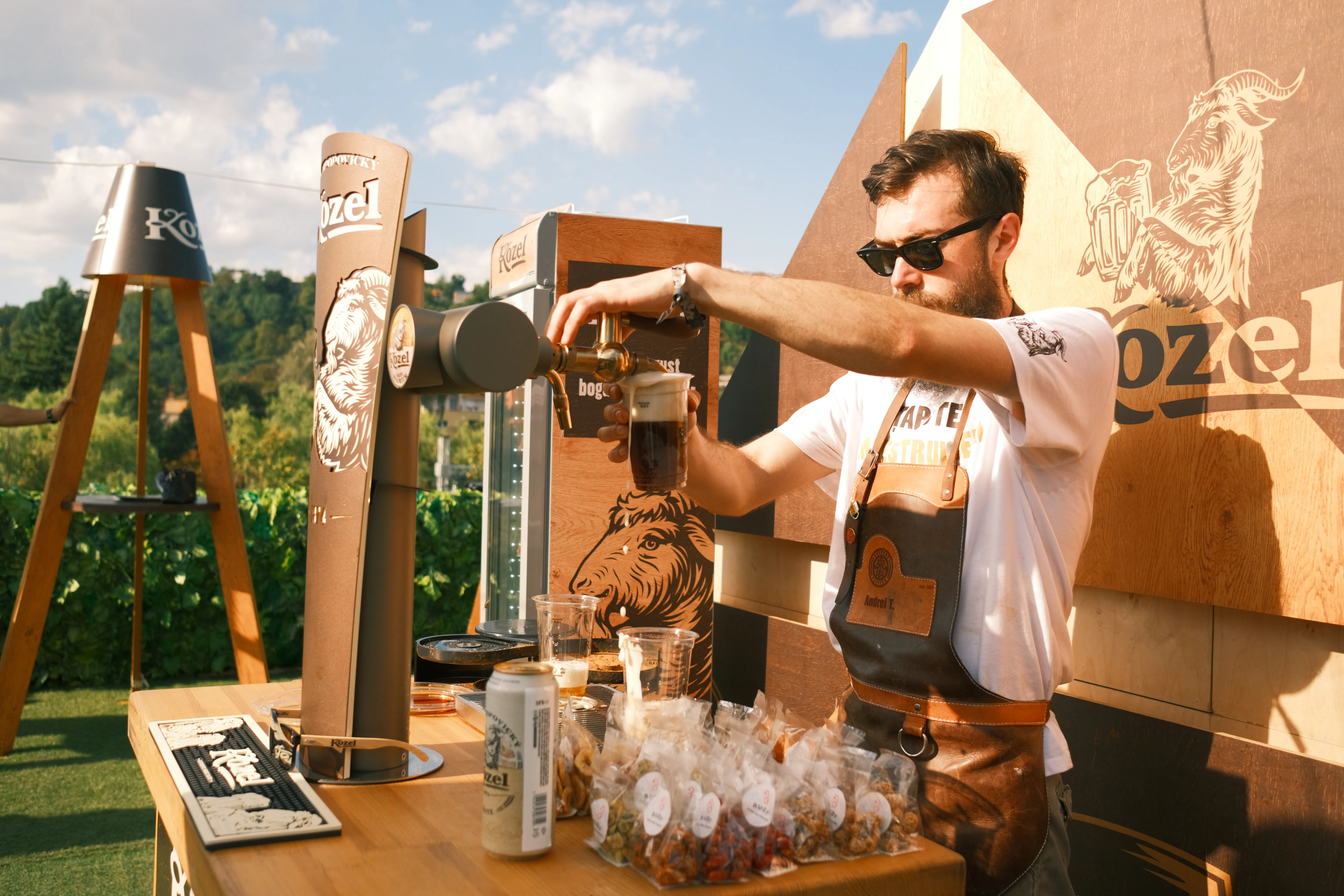 A bartender pours a beer at a branded outdoor bar in warm golden-hour light