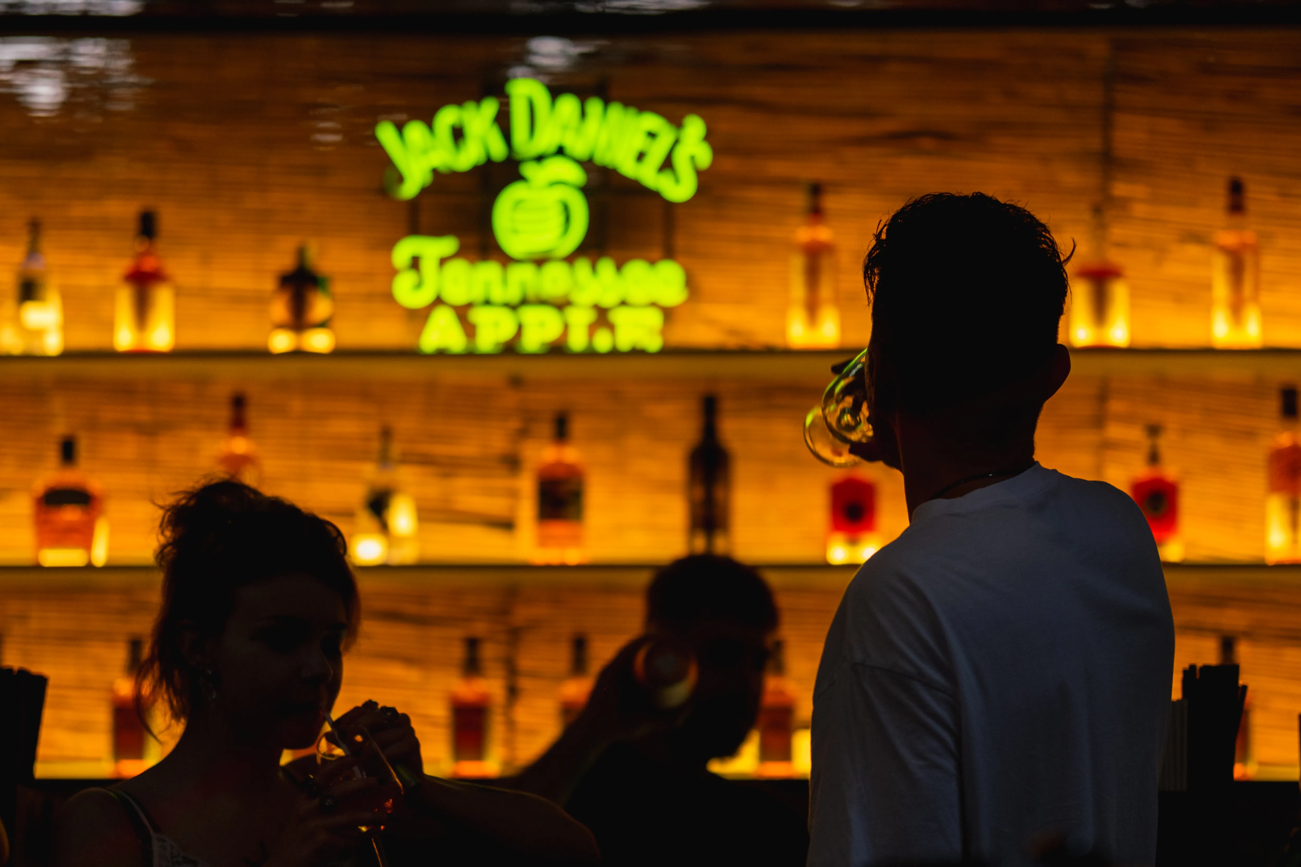 A bar wall lit by a neon Jack Daniel's sign, a figure in silhouette beside it