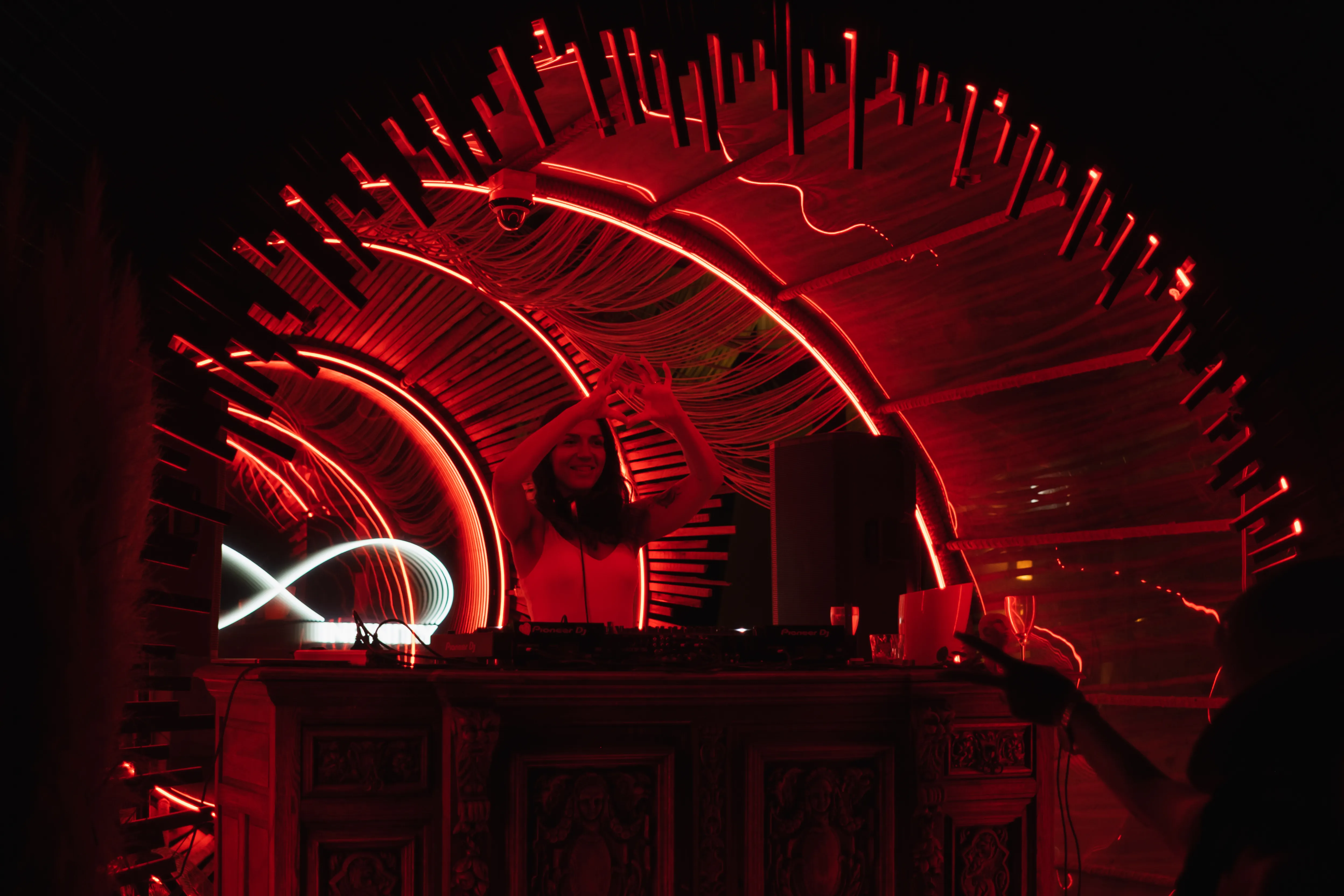 A DJ throws a heart sign beneath a glowing red architectural light installation