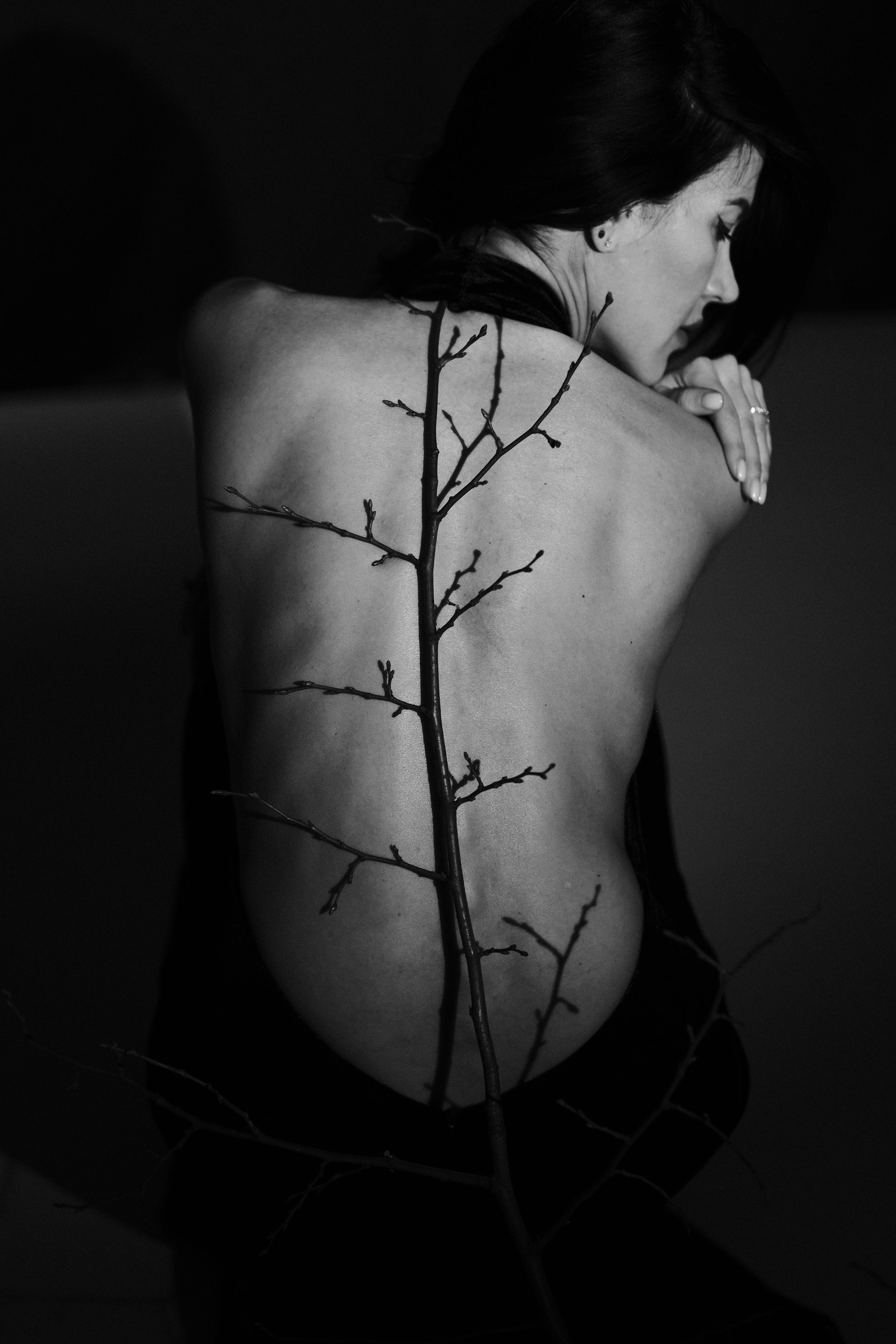 A bare back with a bare tree branch laid horizontally across it, in black and white