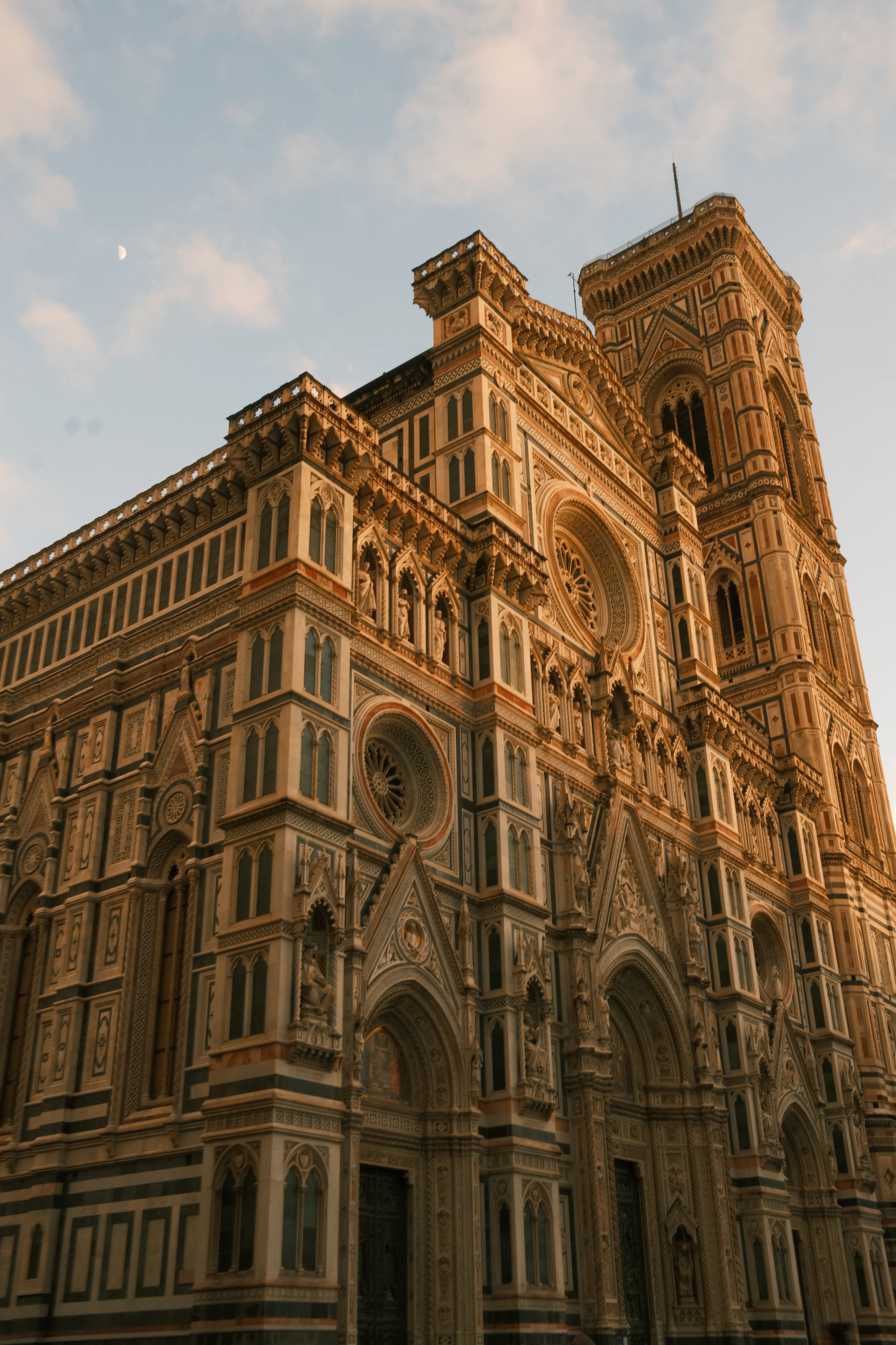 Florence Cathedral facade seen from below at dusk, warm light, the moon visible above