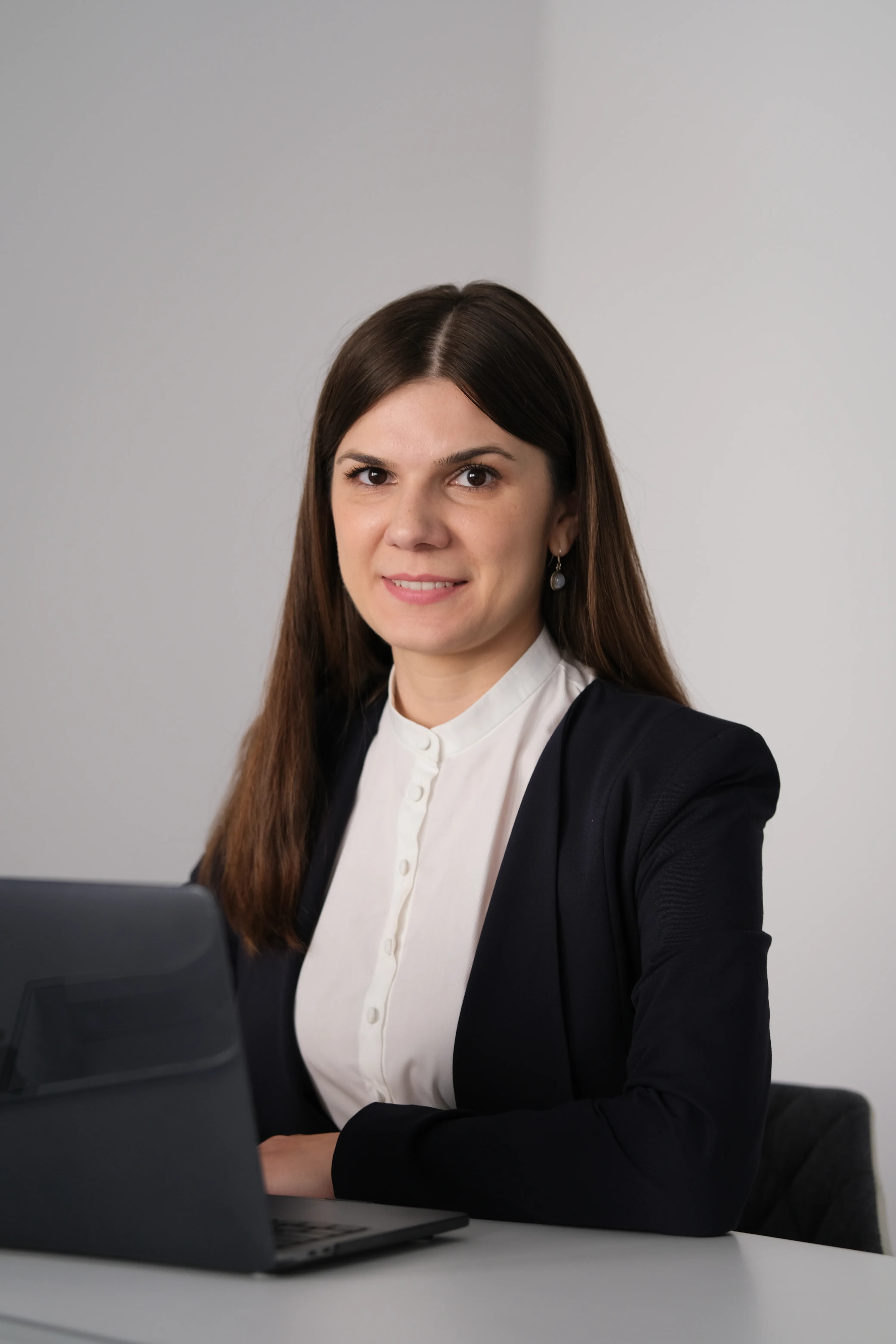 Woman in a navy blazer in an office, laptop open beside her, looking away from camera