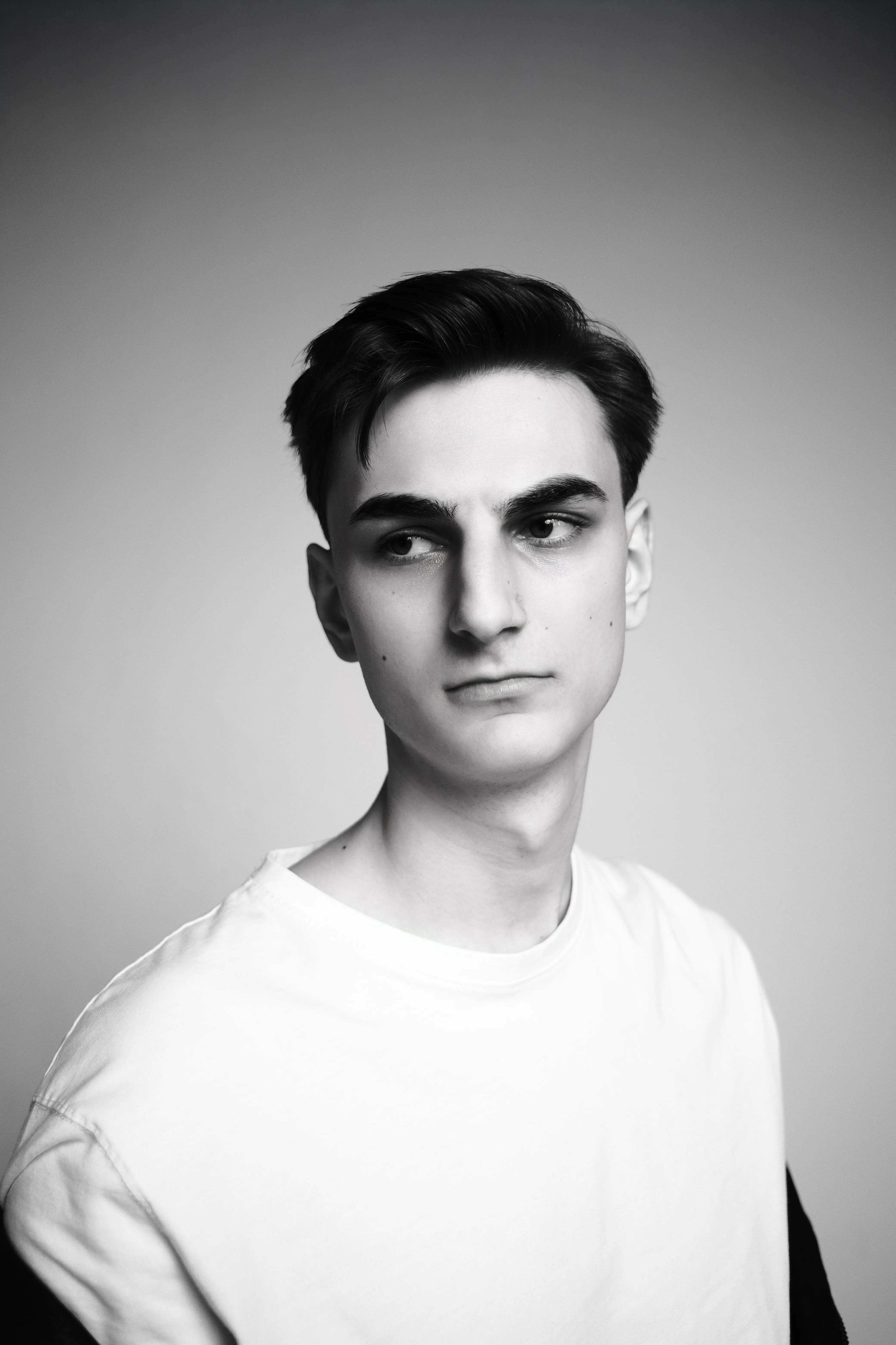 Black and white studio headshot of a young man in a white t-shirt, looking off-camera