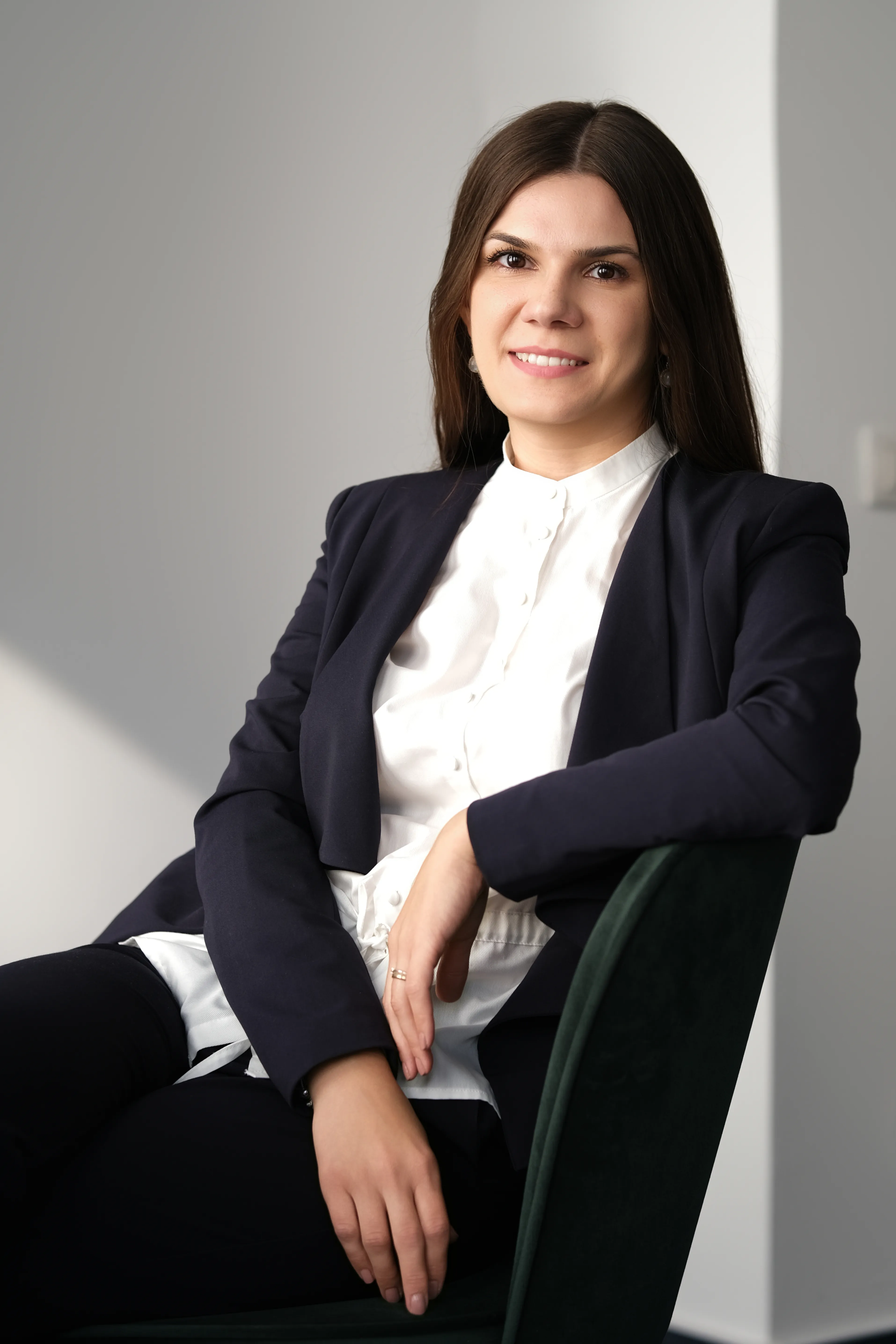 Woman in a navy blazer smiling, arm resting on a green velvet chair