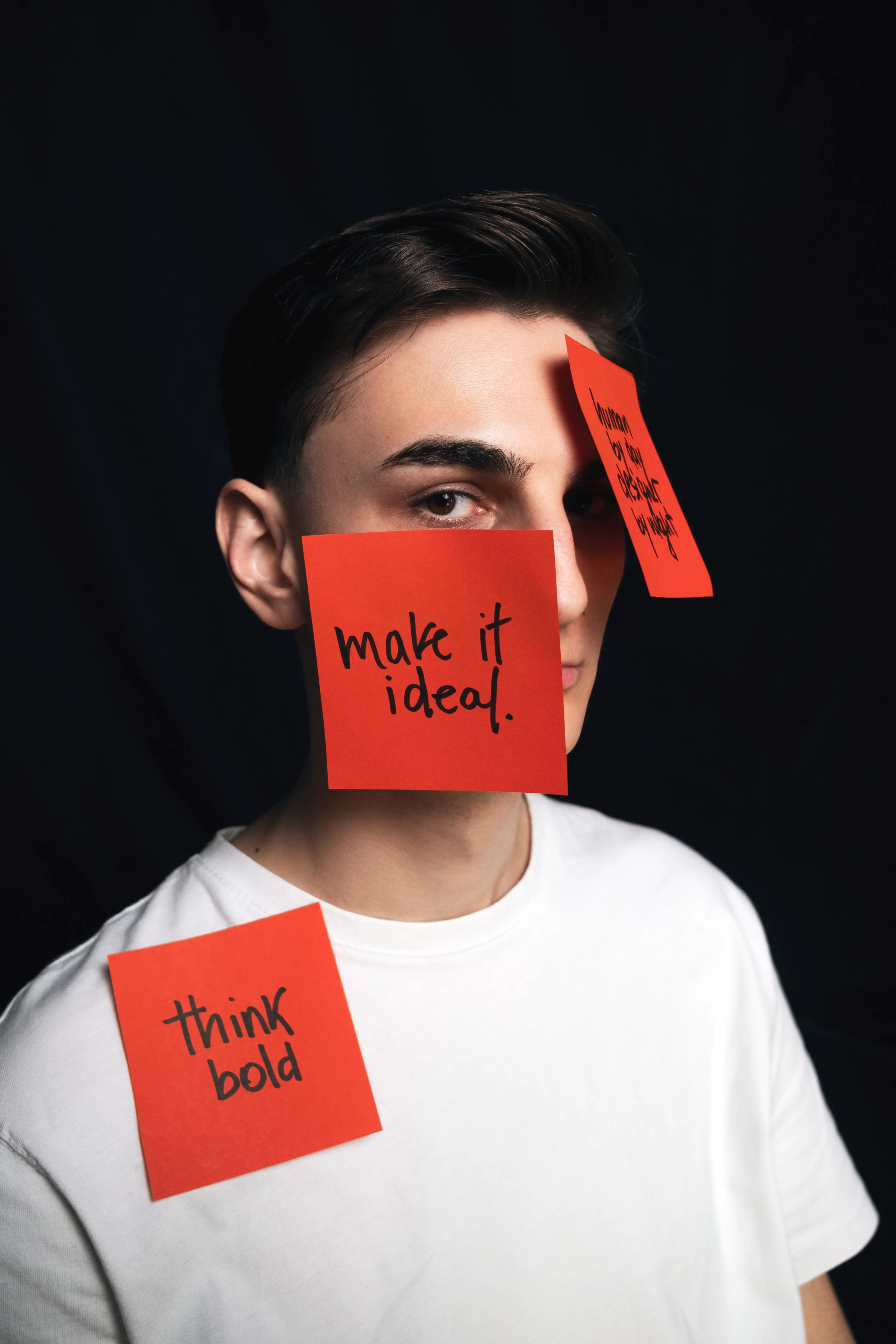 Man with handwritten red sticky notes reading 'make it ideal' and 'think bold' placed on his face and shoulder