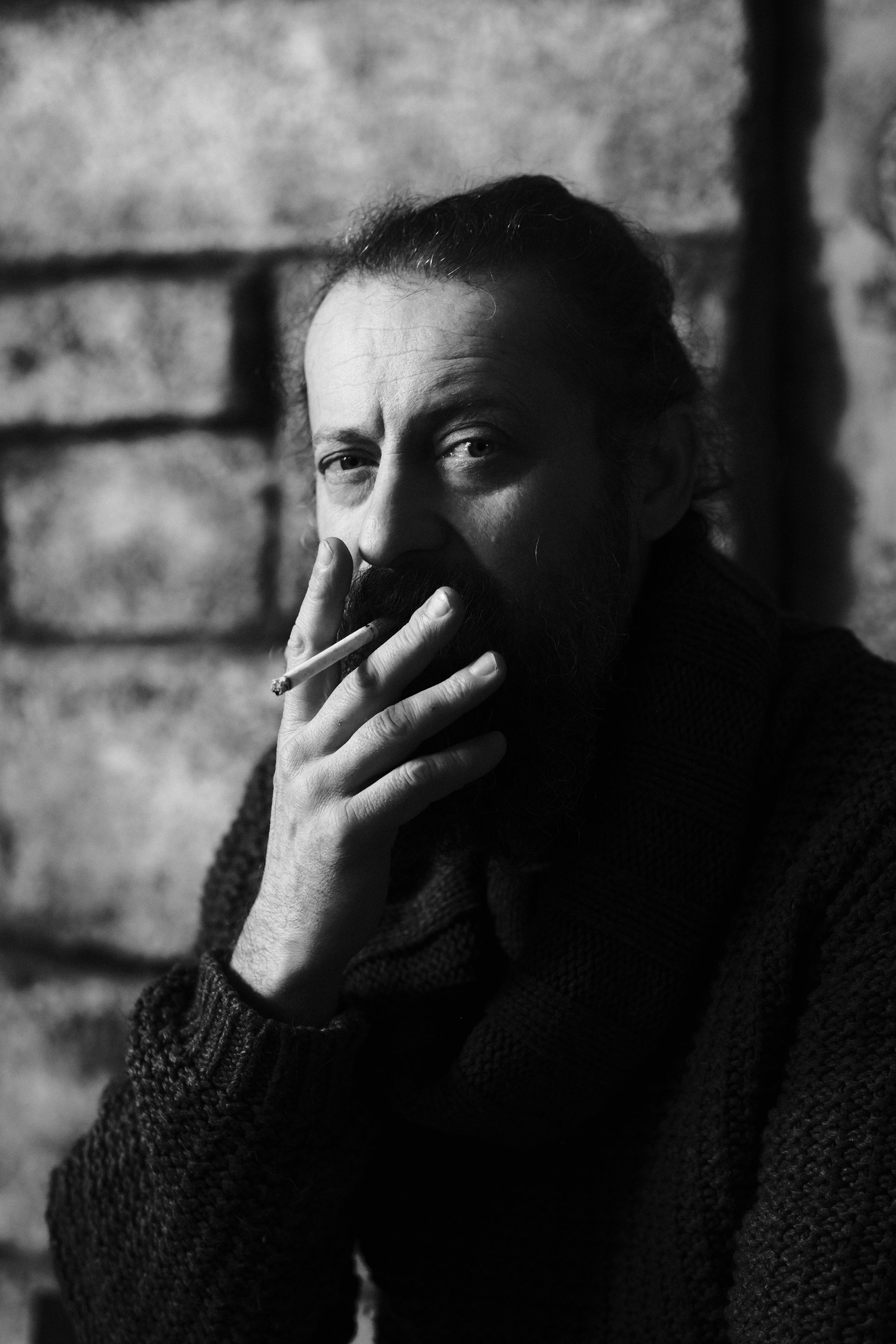 Black and white portrait, cigarette in hand, direct gaze, brick wall background