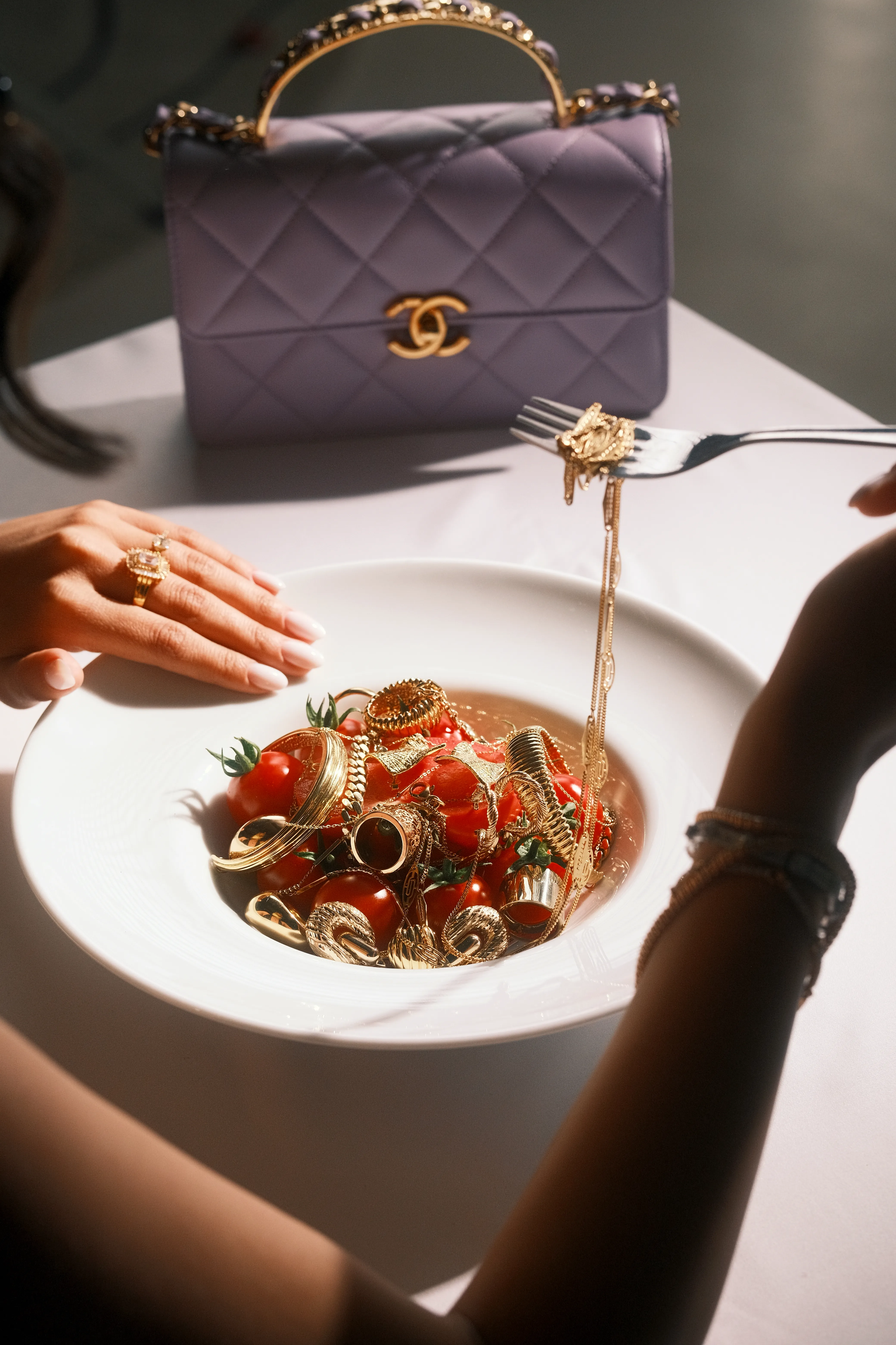 Jewelry spilling across a plate of cherry tomatoes beside a quilted handbag