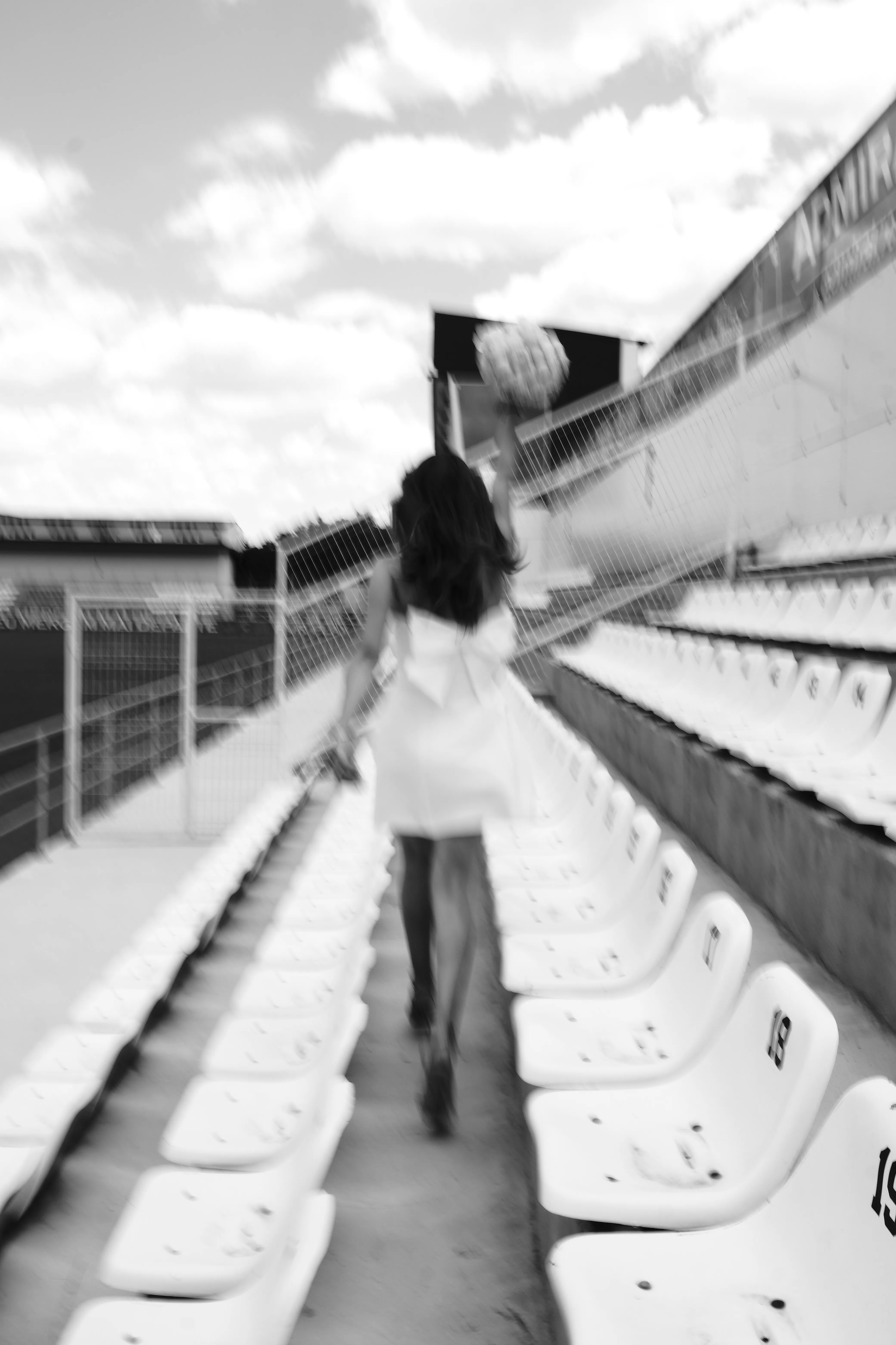 A bride walking away down a symmetric row of stadium seats, bouquet raised, black and white
