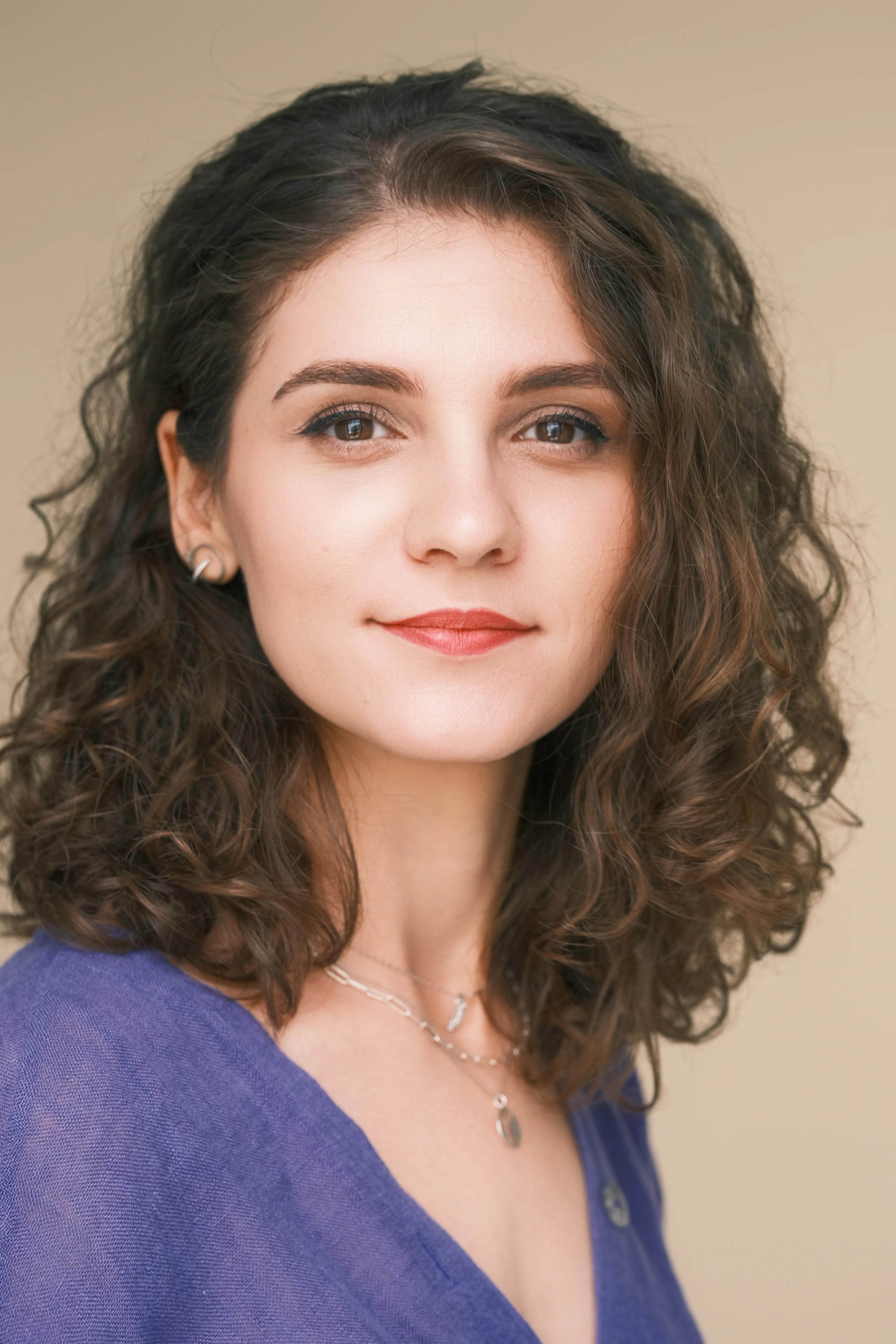 Woman with curly hair, soft smile, warm beige studio background