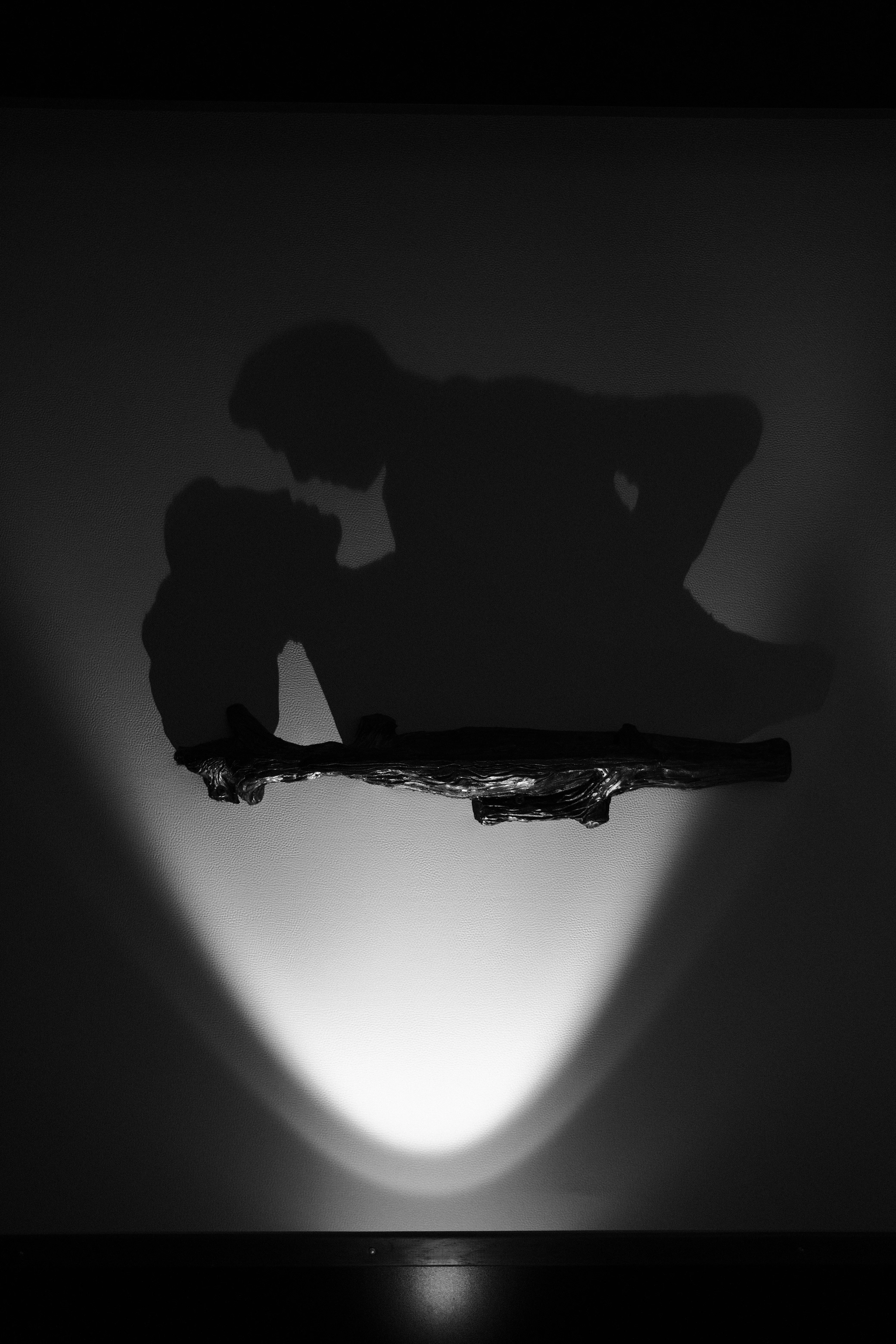 A silhouetted figure bent low under a single dramatic spotlight, black and white