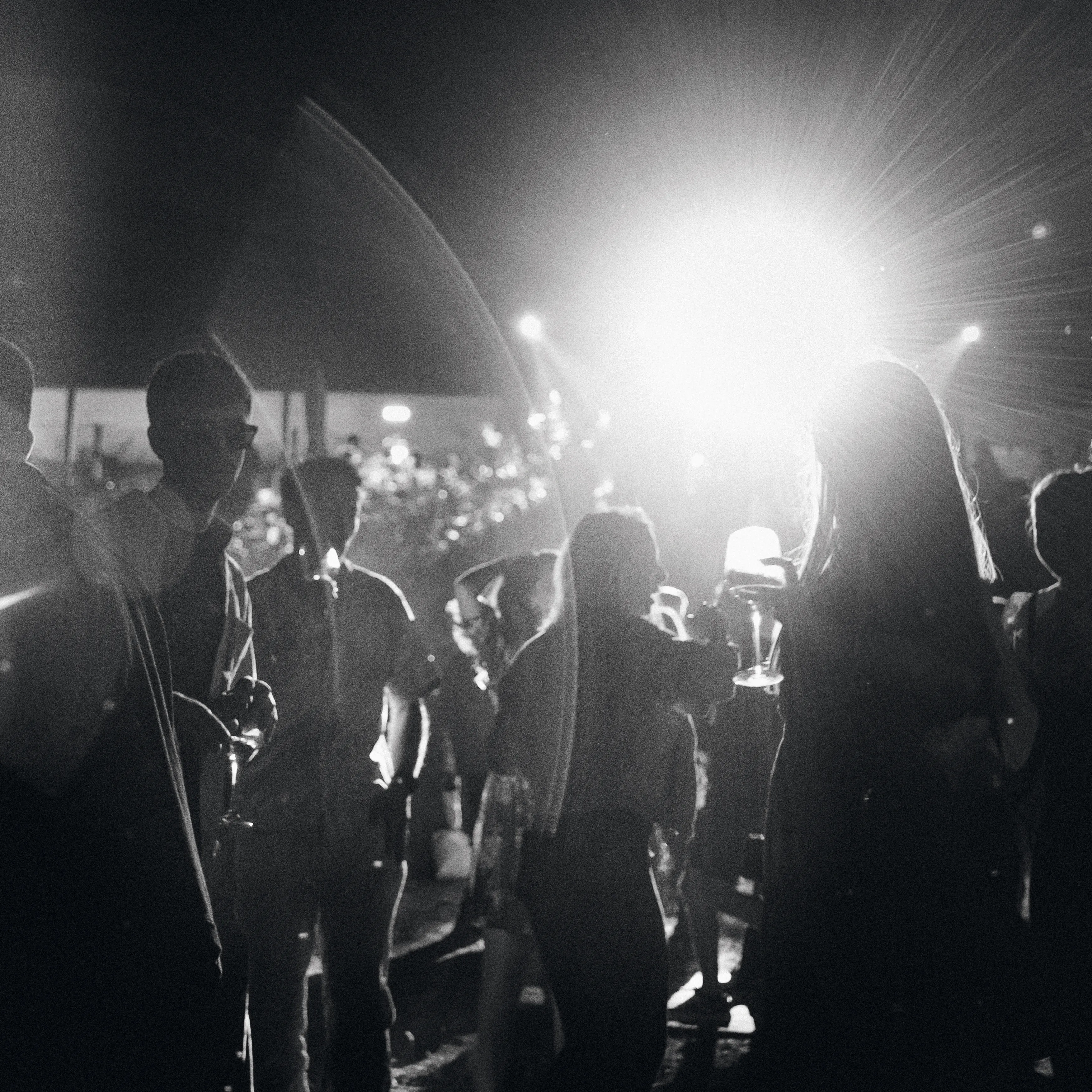 A group backlit by a dramatic lens flare, silhouettes against bursting light, black and white