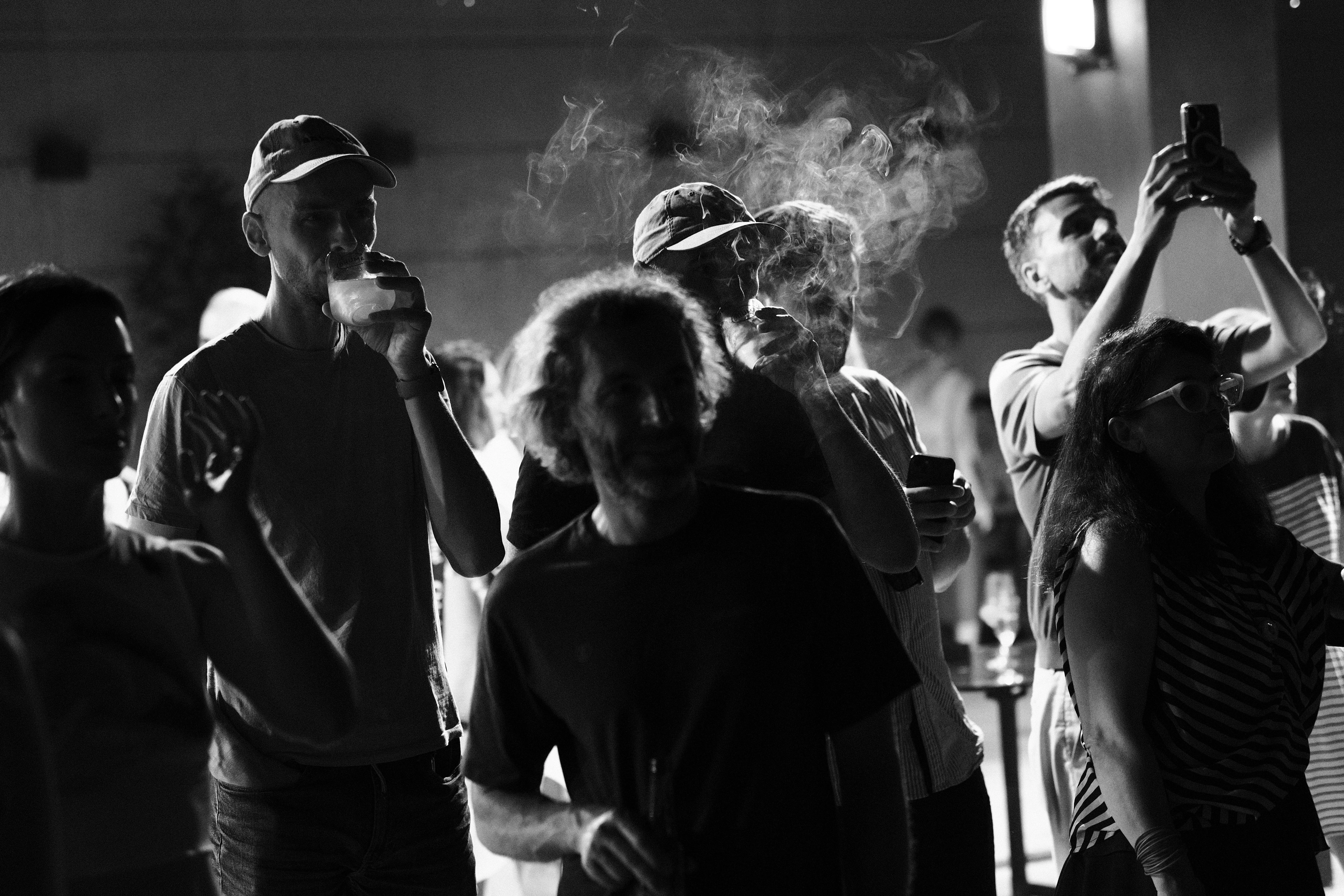 A crowd backlit by cigarette smoke and raised phones, black and white