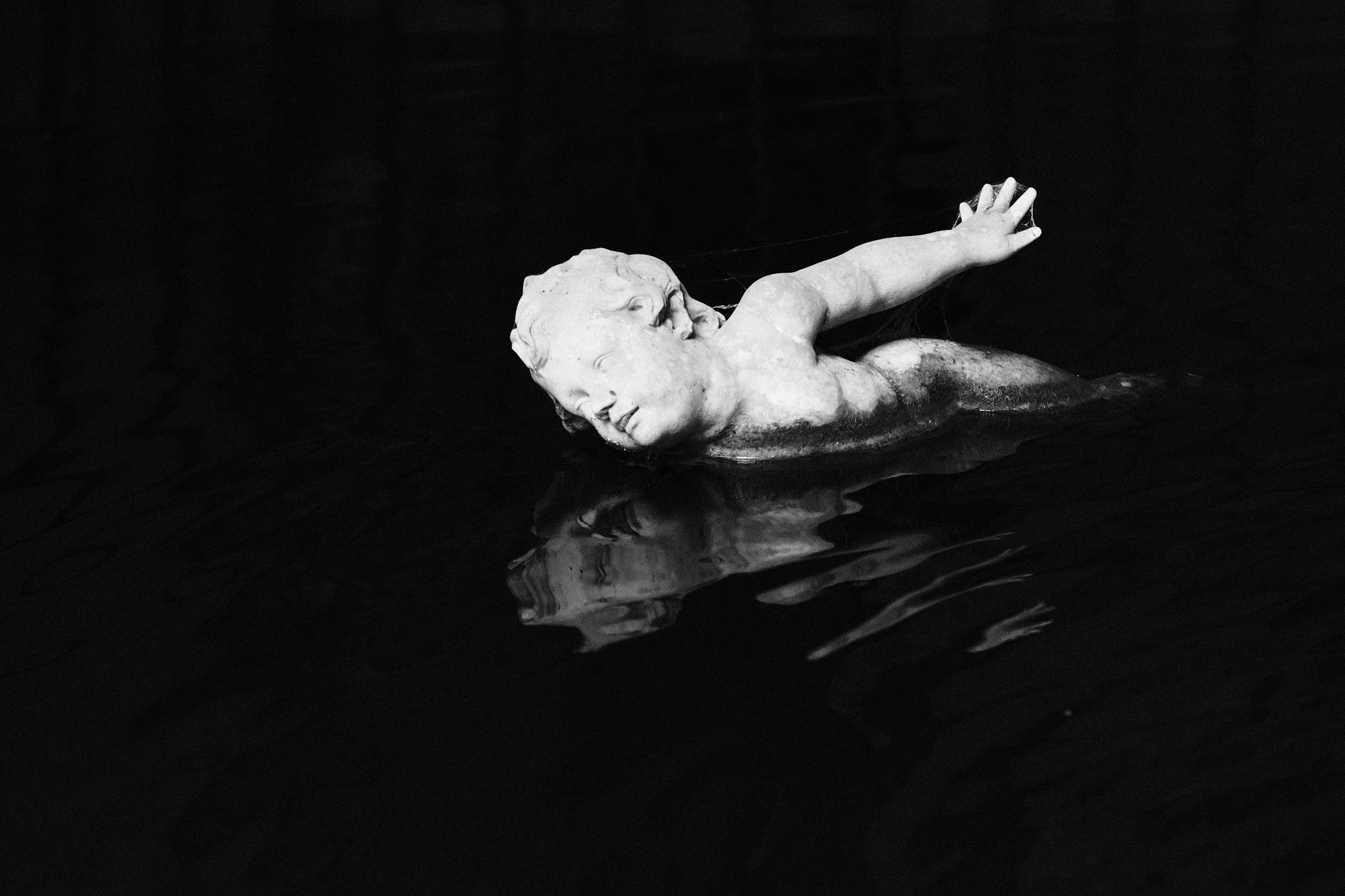 A figure floating in dark water, reflected in the surface, black and white