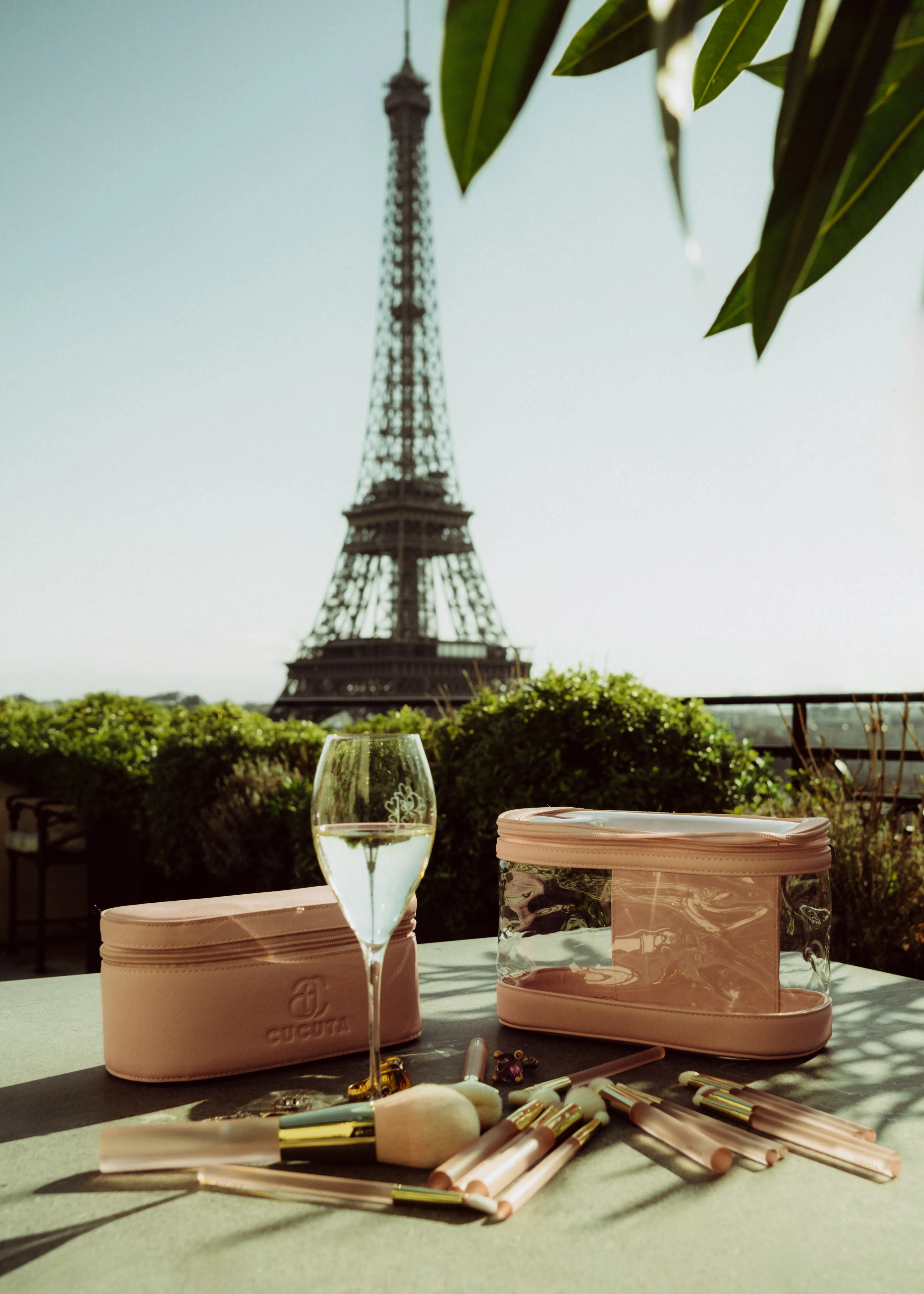 A rooftop table with beauty cases, makeup brushes, and a glass of champagne, the Eiffel Tower visible in the background