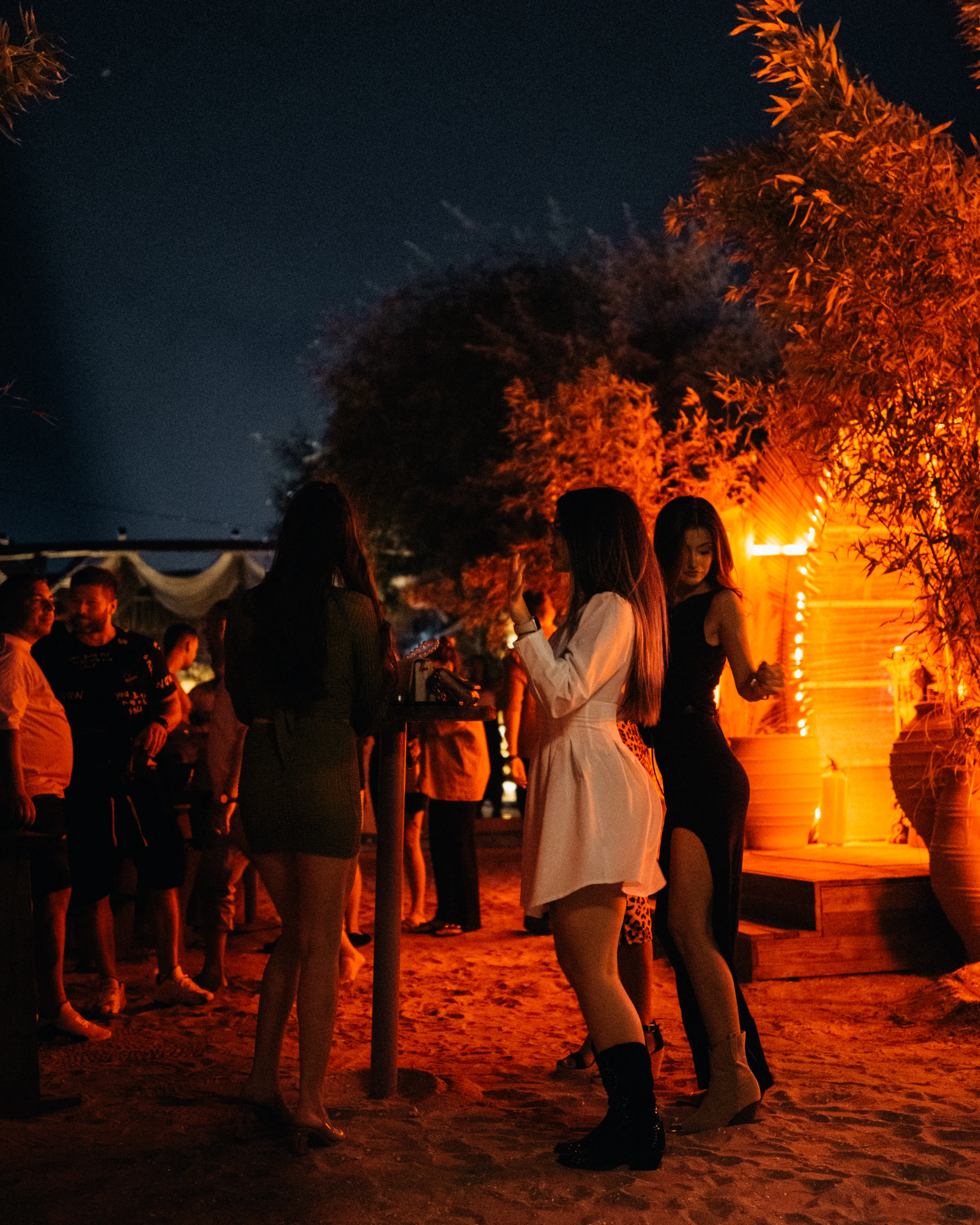 A group of women dancing together at night under warm string lights