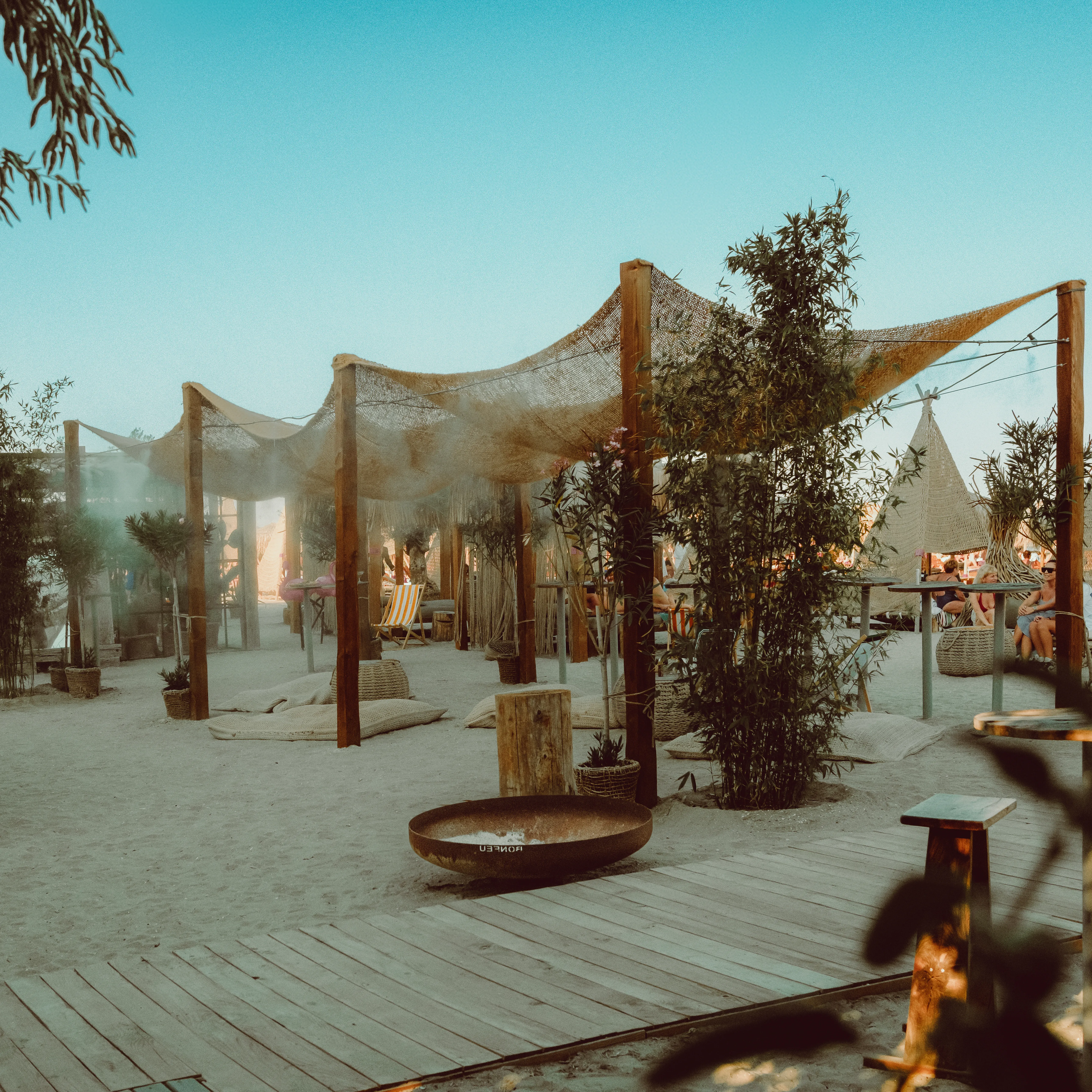 Empty daybeds under thatched canopies at Infinity Beach under a clear blue sky