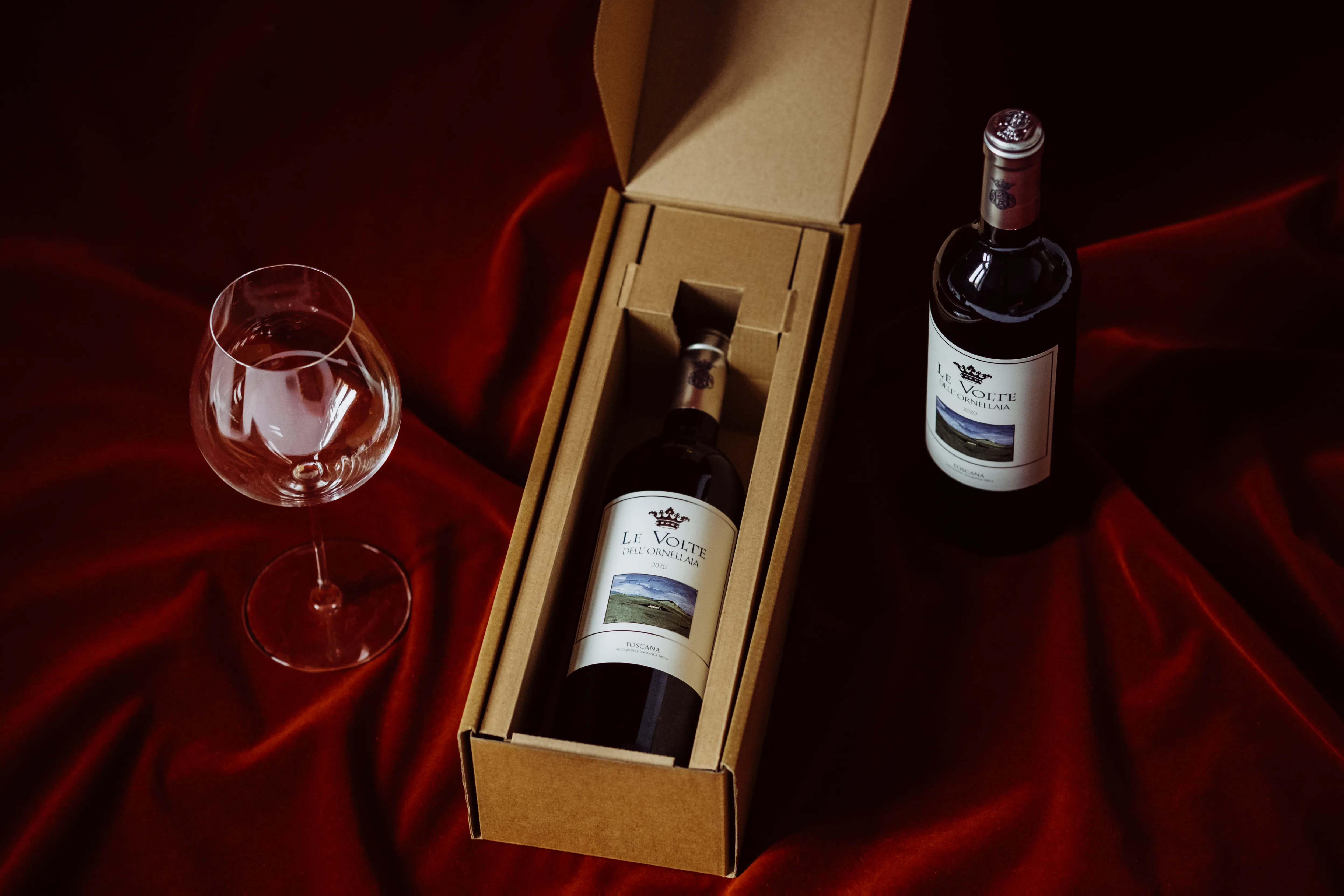 Two wine bottles on dark red velvet with a wine glass, dramatic lighting