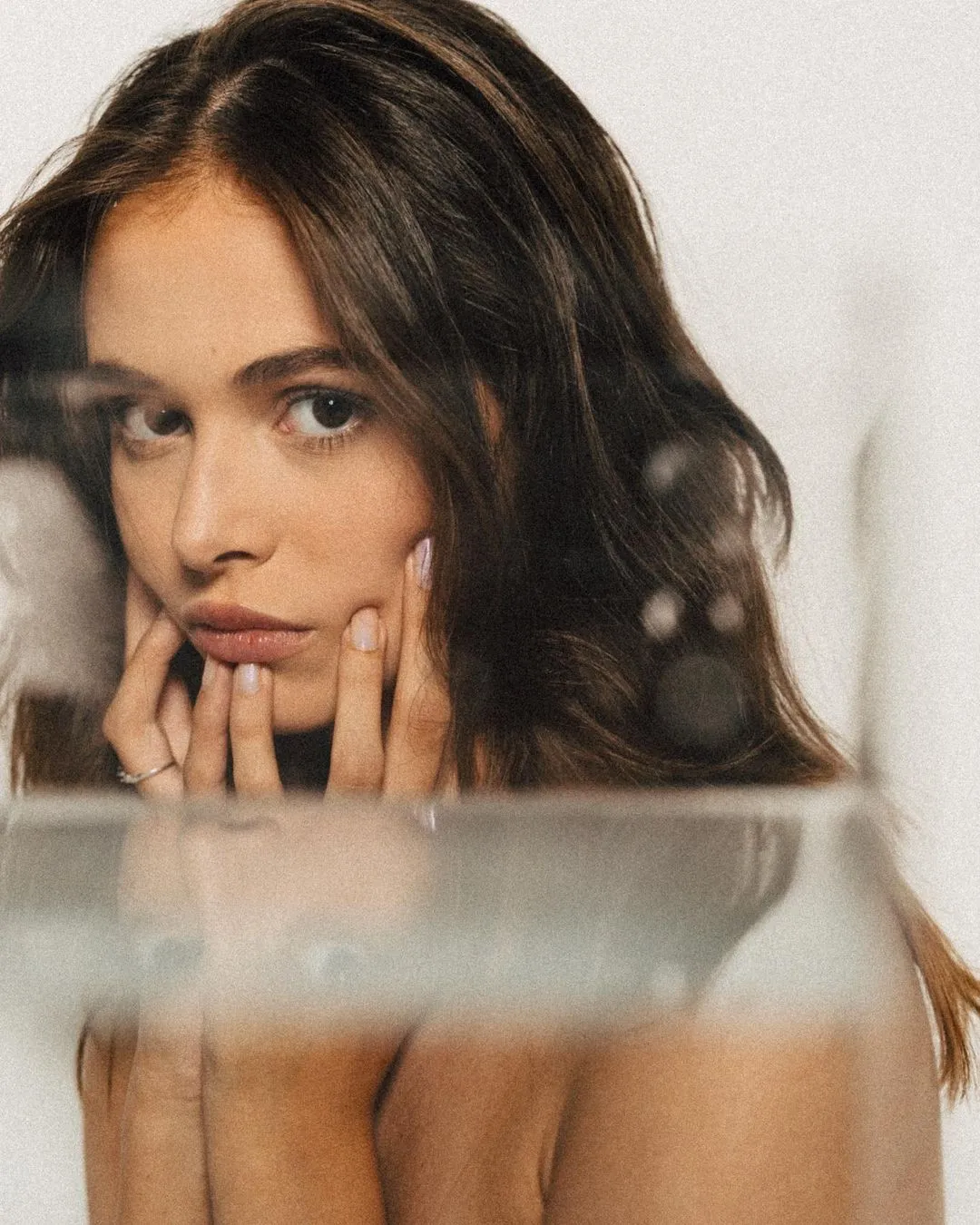 Close-up portrait of a woman resting her chin on her hands, glass reflection in the foreground