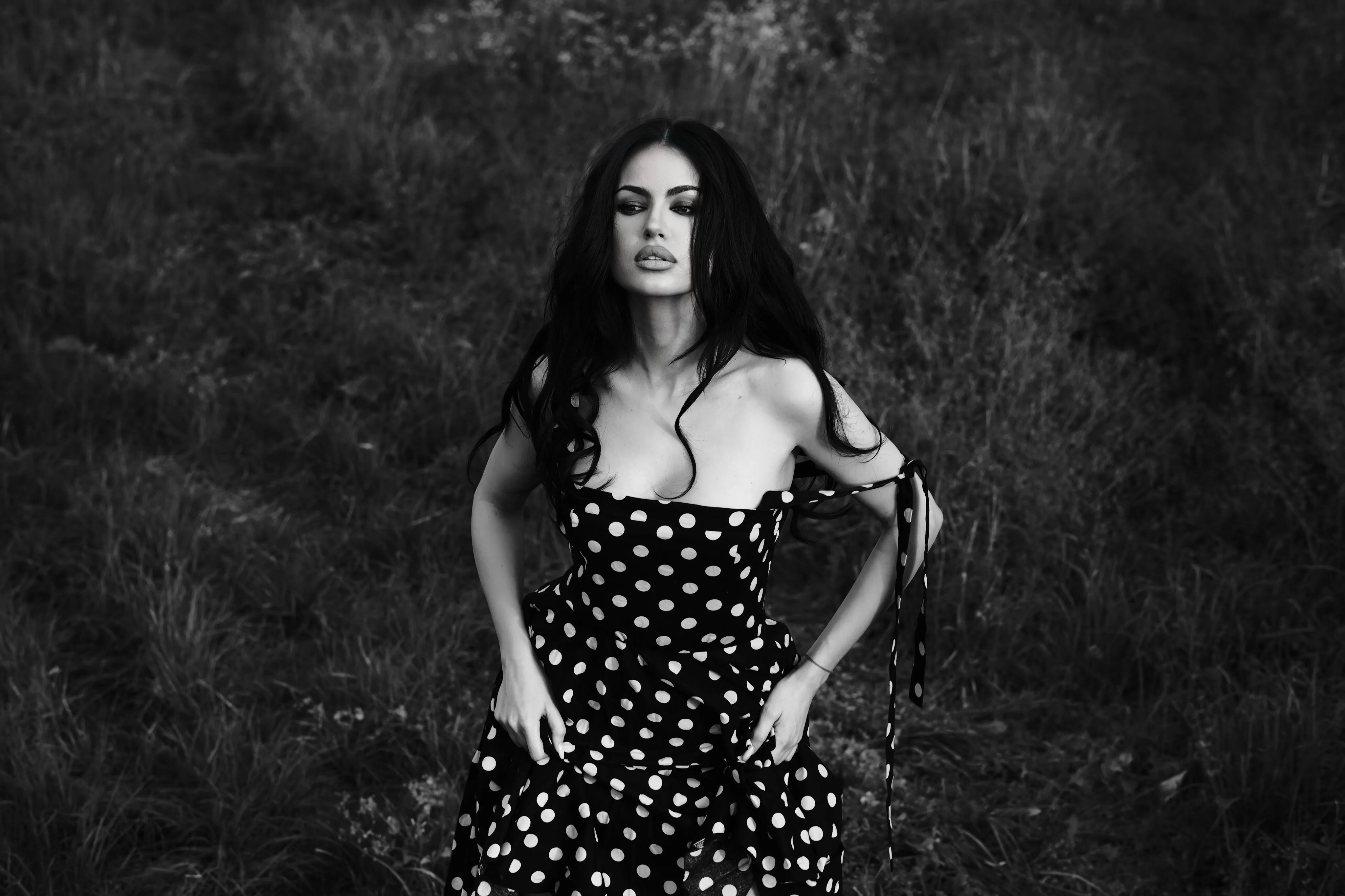 Black and white portrait in a polka dot dress, direct gaze, tall grass background