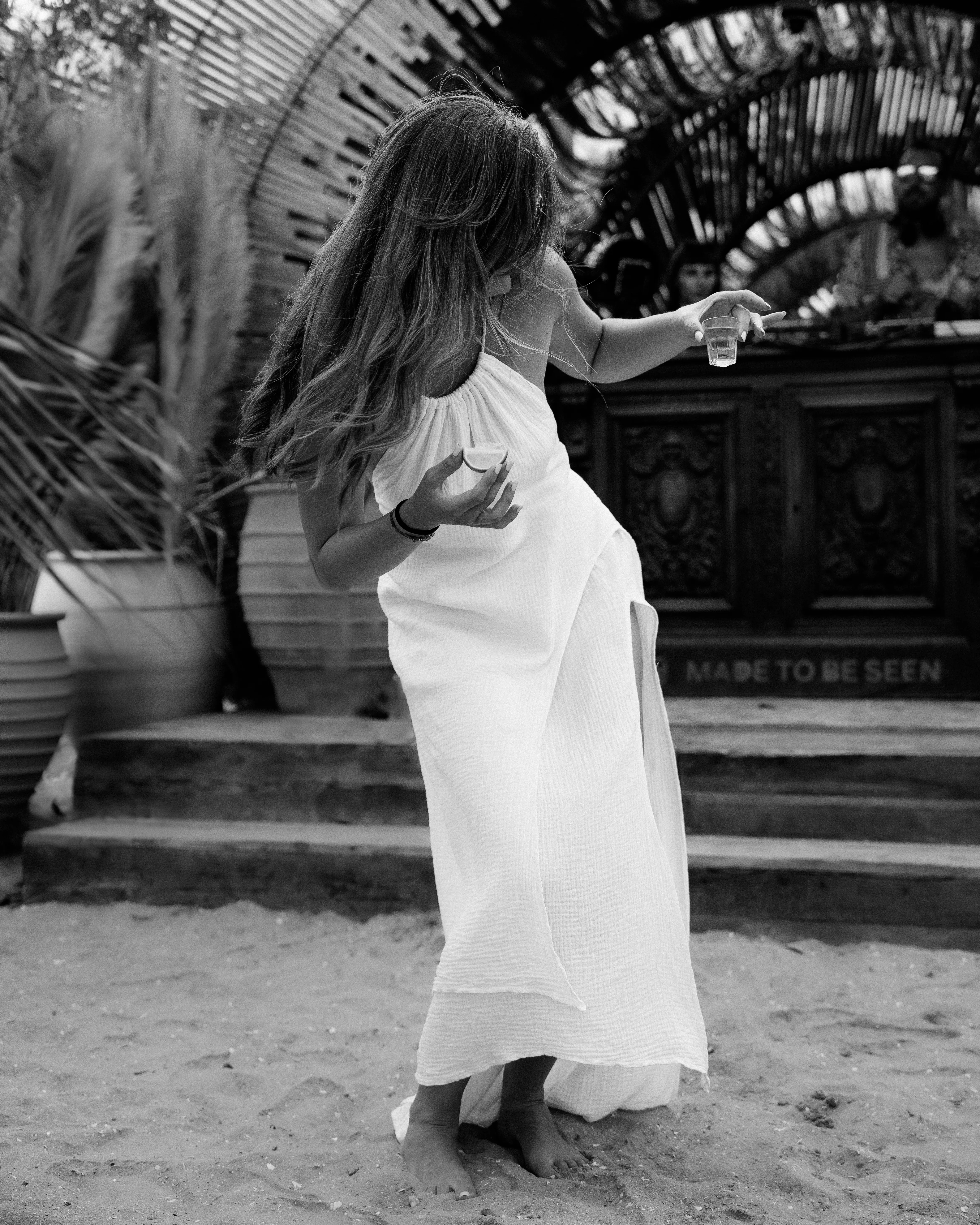 Black and white photo of a woman twirling in a dress, drink in hand