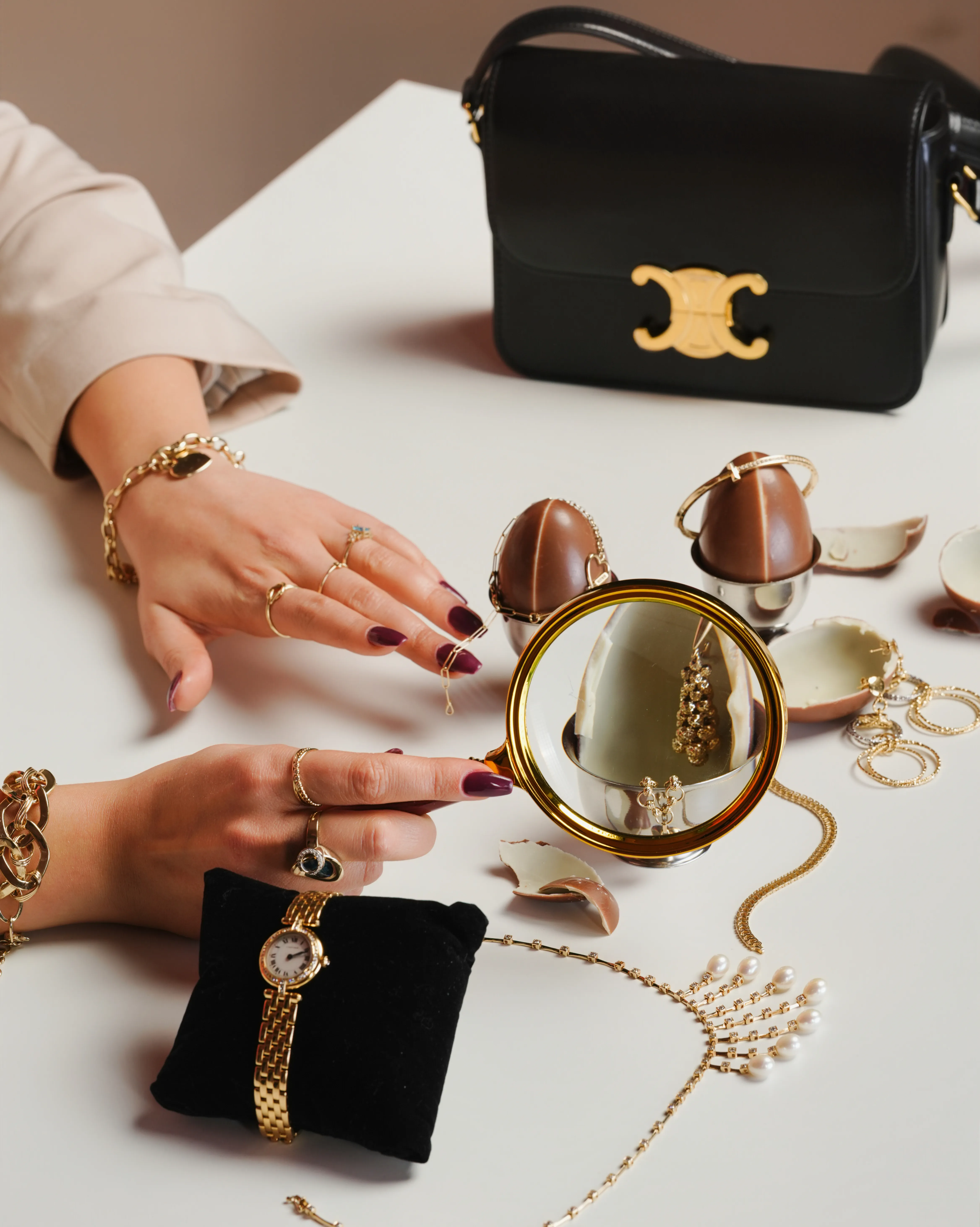 A cracked chocolate egg reveals jewelry inside, seen through a gold-rimmed magnifying glass