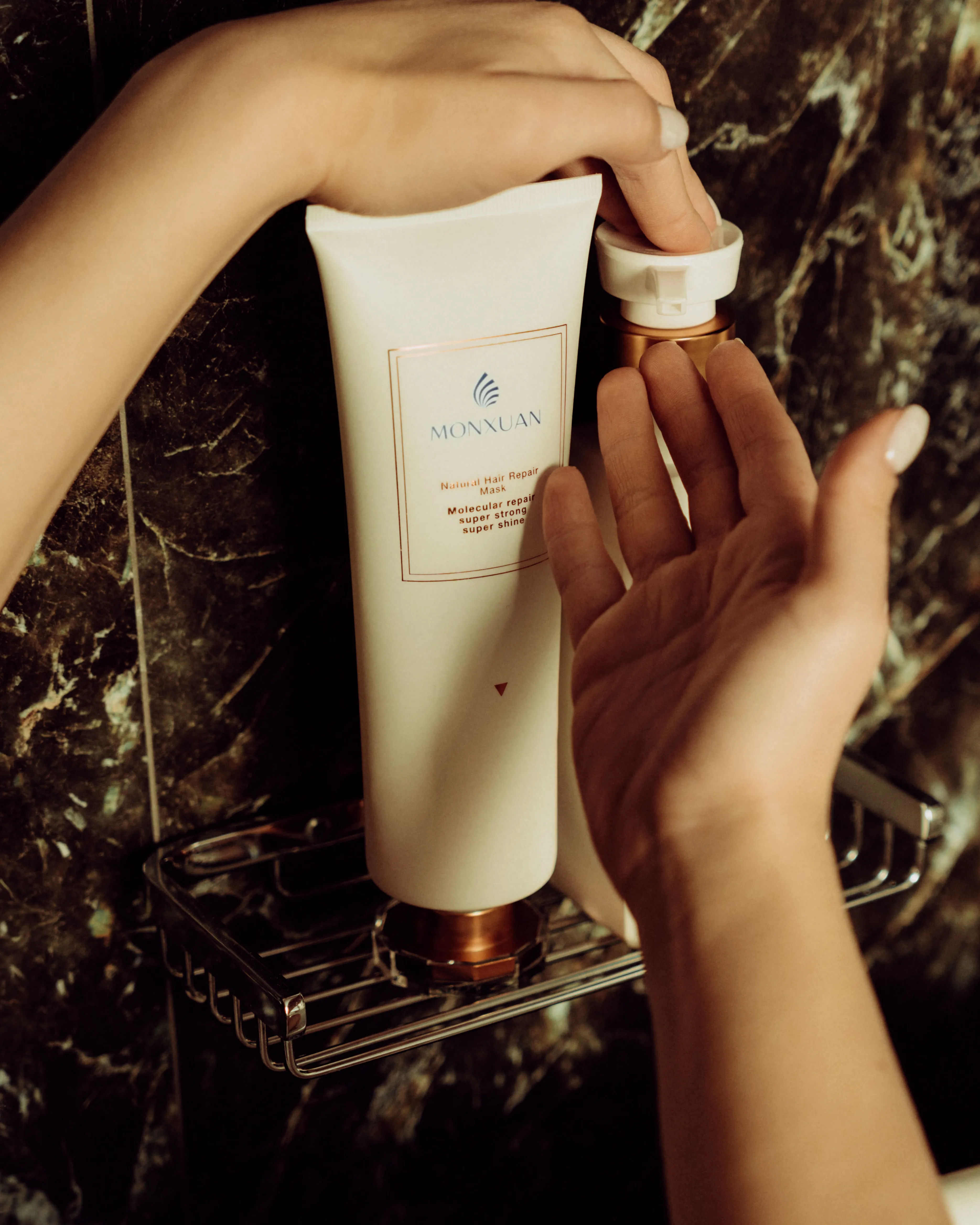 A haircare product tube held against a dark marble bathroom wall, warm cinematic light