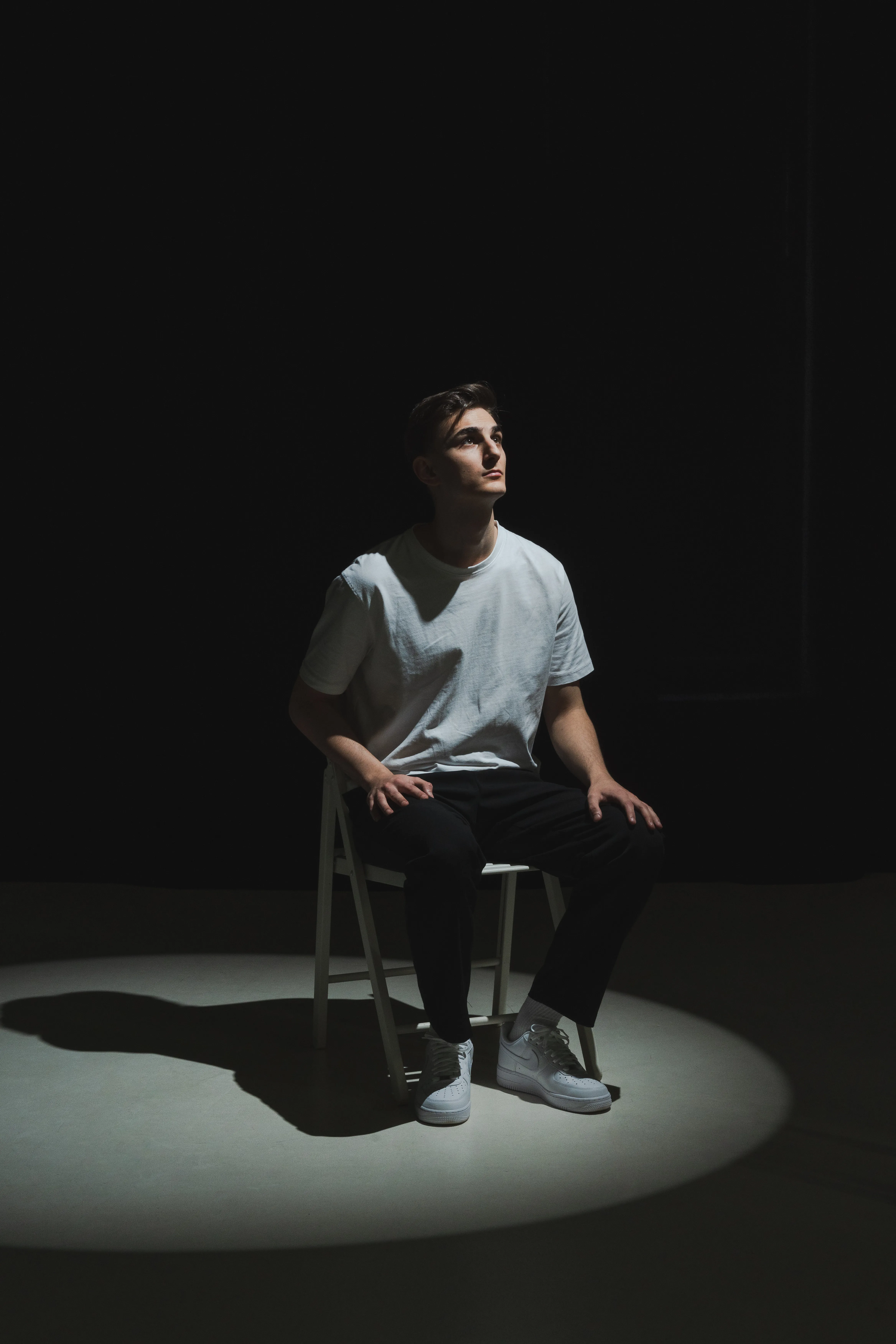 Black and white studio portrait, seated young man under a single spotlight