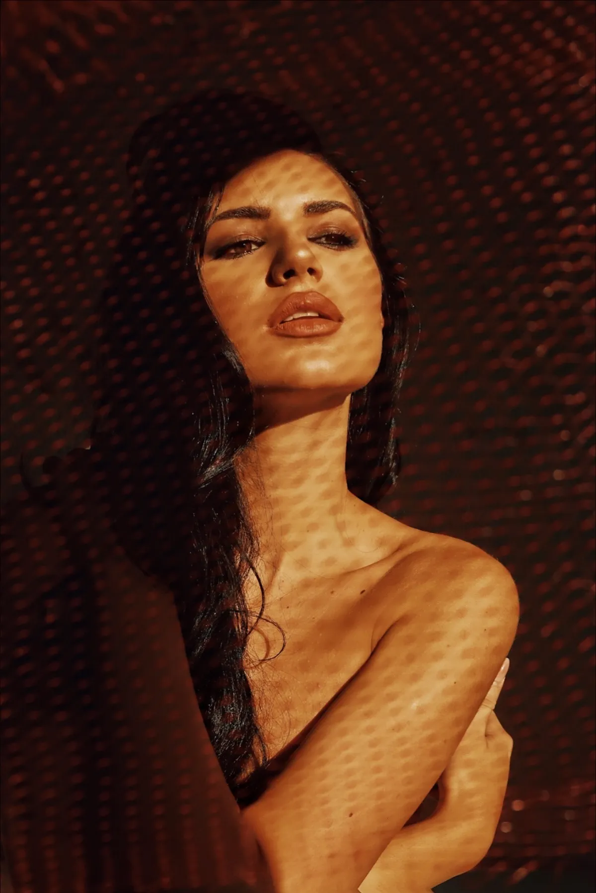 Lumină cu model de grilă cade pe umărul și clavicula unei femei, ca niște curbe de nivel pe o hartă
