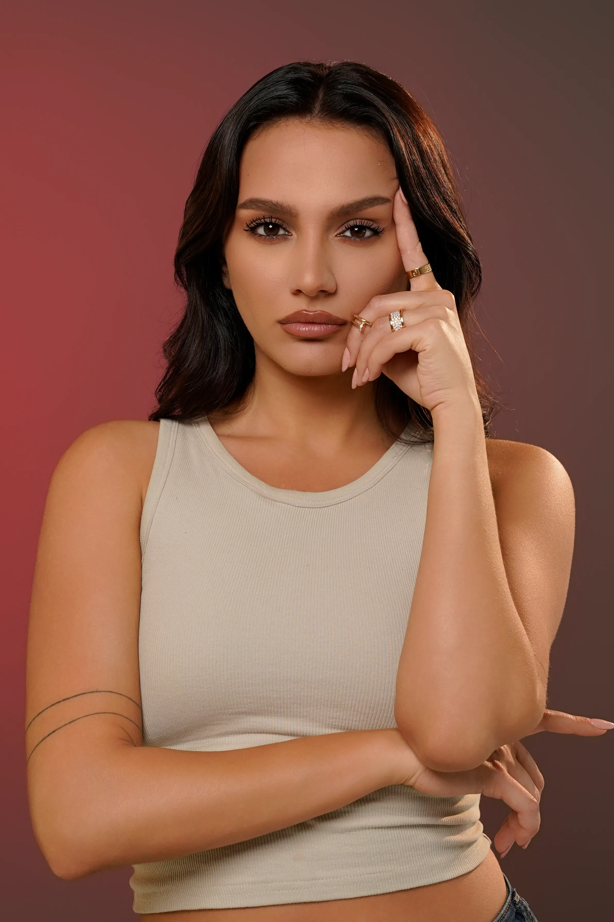 Close-up portrait of a woman against a warm red-to-brown gradient background, hand near her face