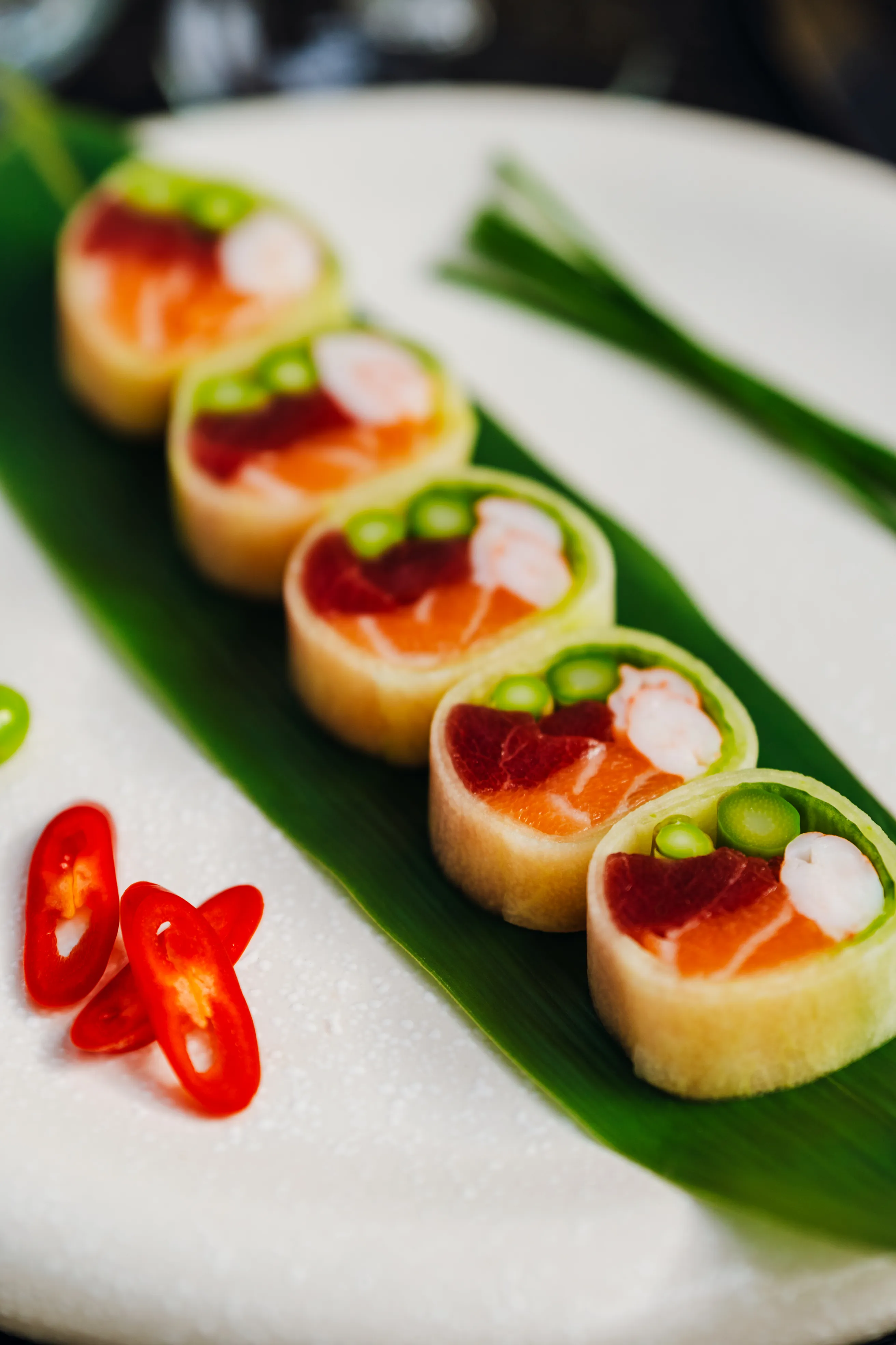 A row of canapé bites with salmon and chili on a banana leaf
