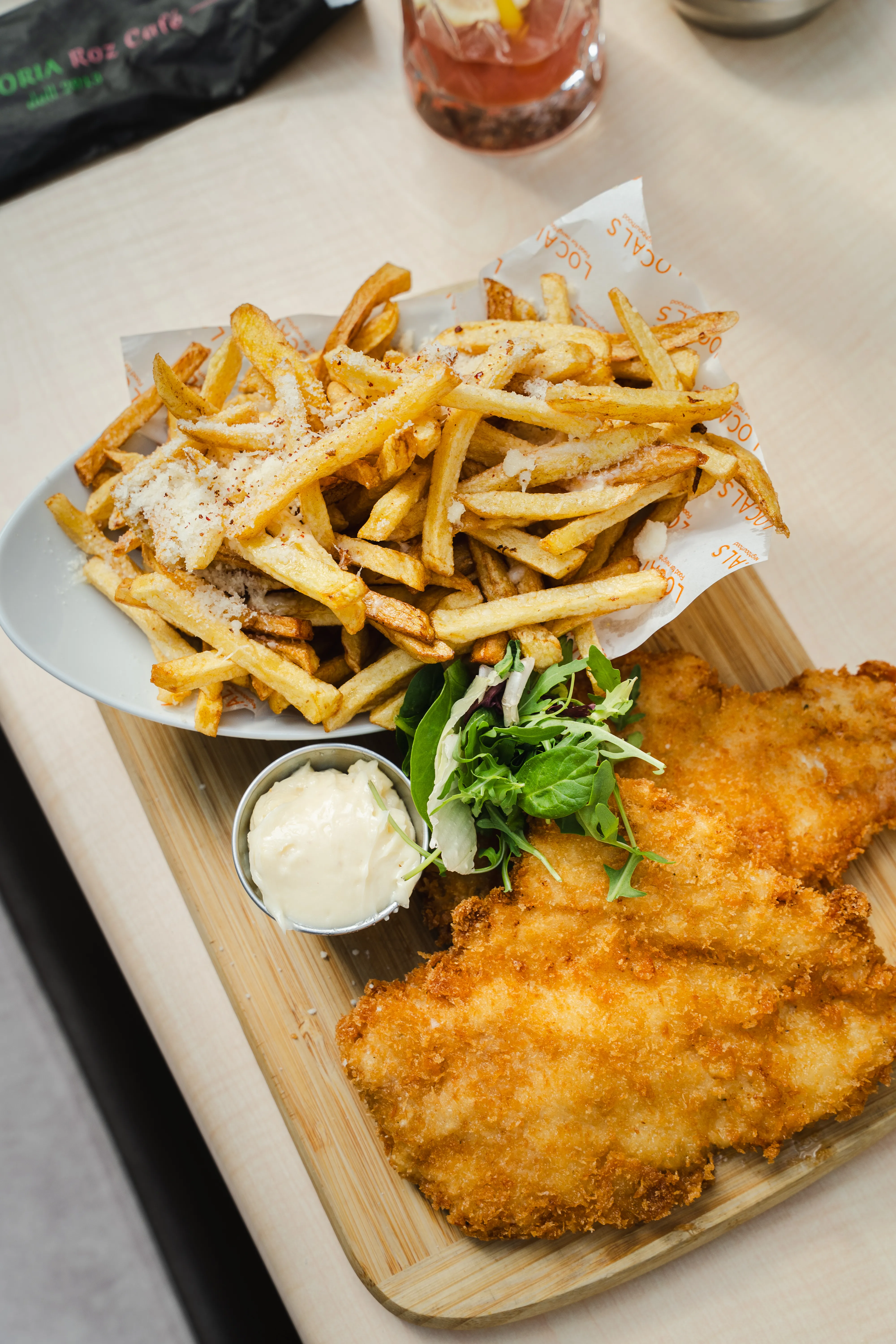 A plate of parmesan fries with a breaded cutlet, greens, and a dipping sauce