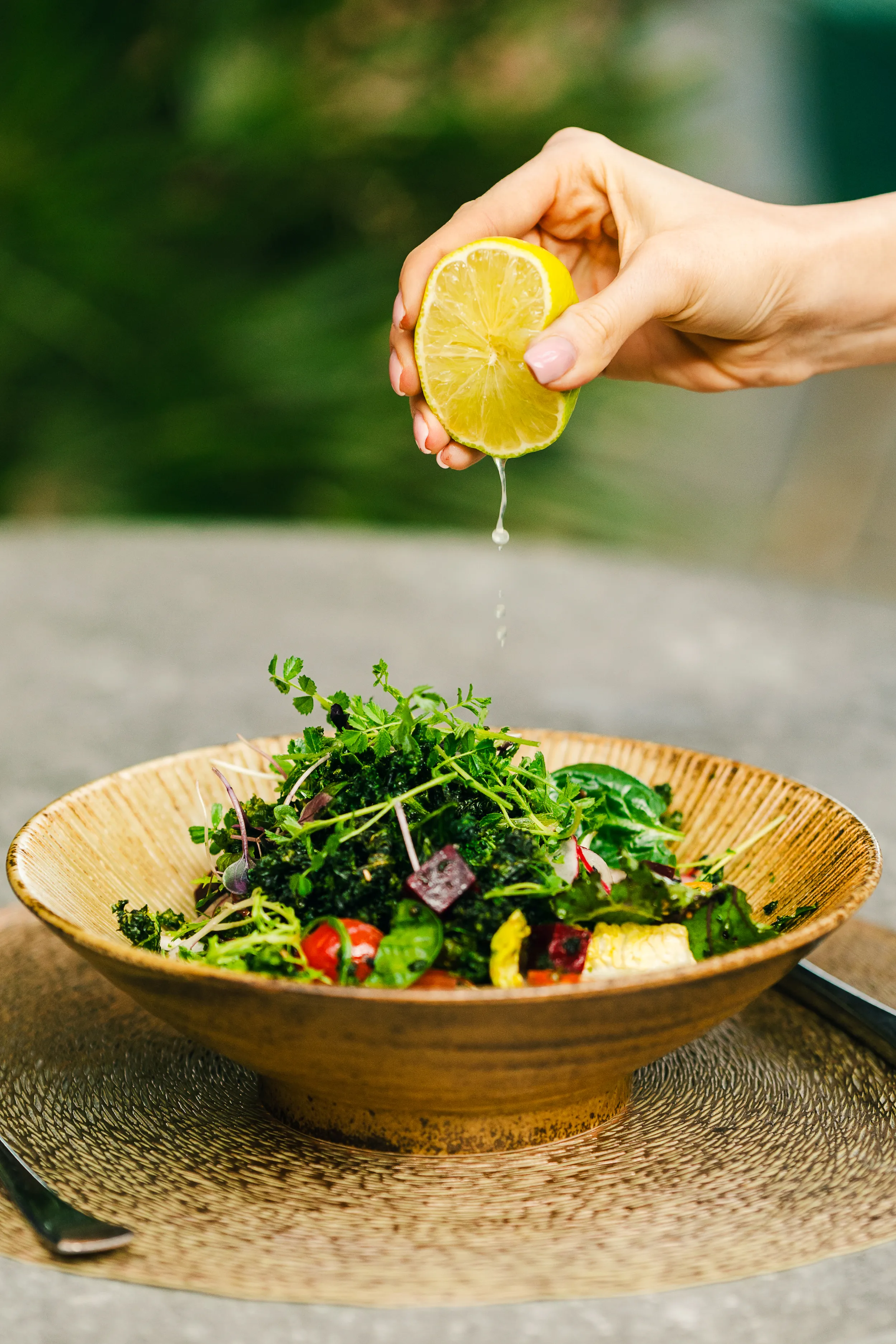 A hand squeezes a lemon half over a bowl of leafy salad