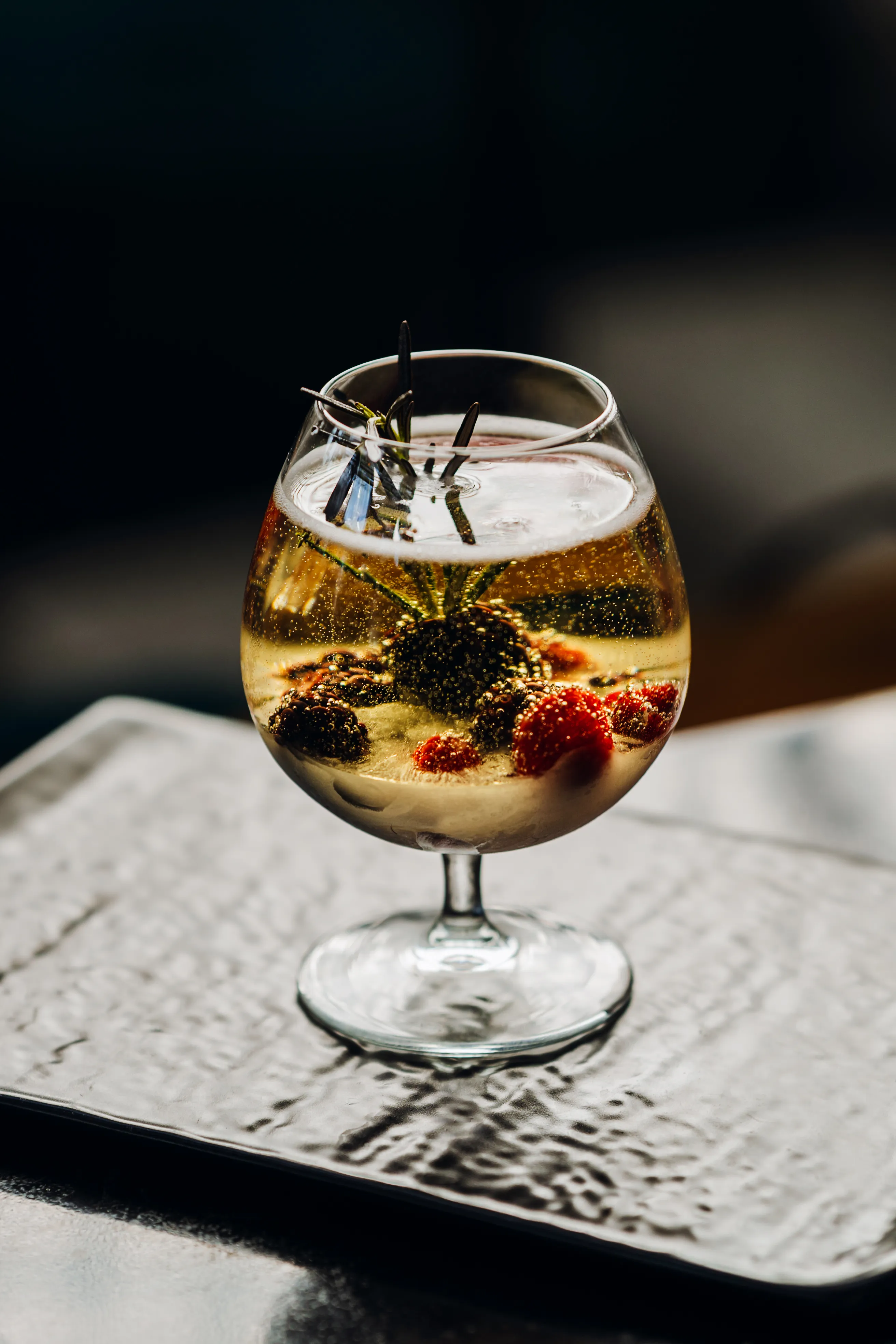 A cocktail glass with a frozen flower ice sphere, lit dramatically against a dark background