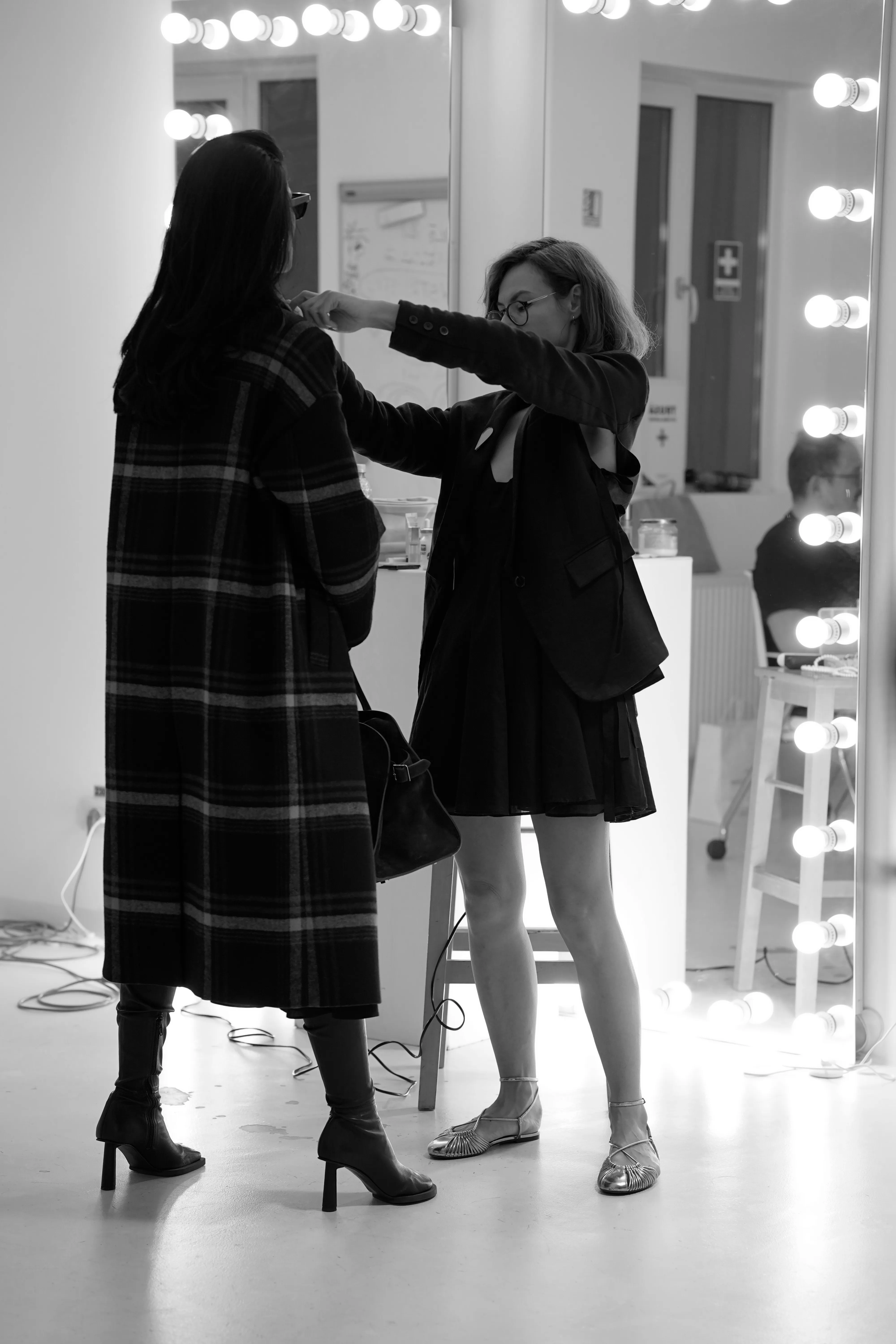Black and white candid of a stylist adjusting a model's coat in front of a lit mirror