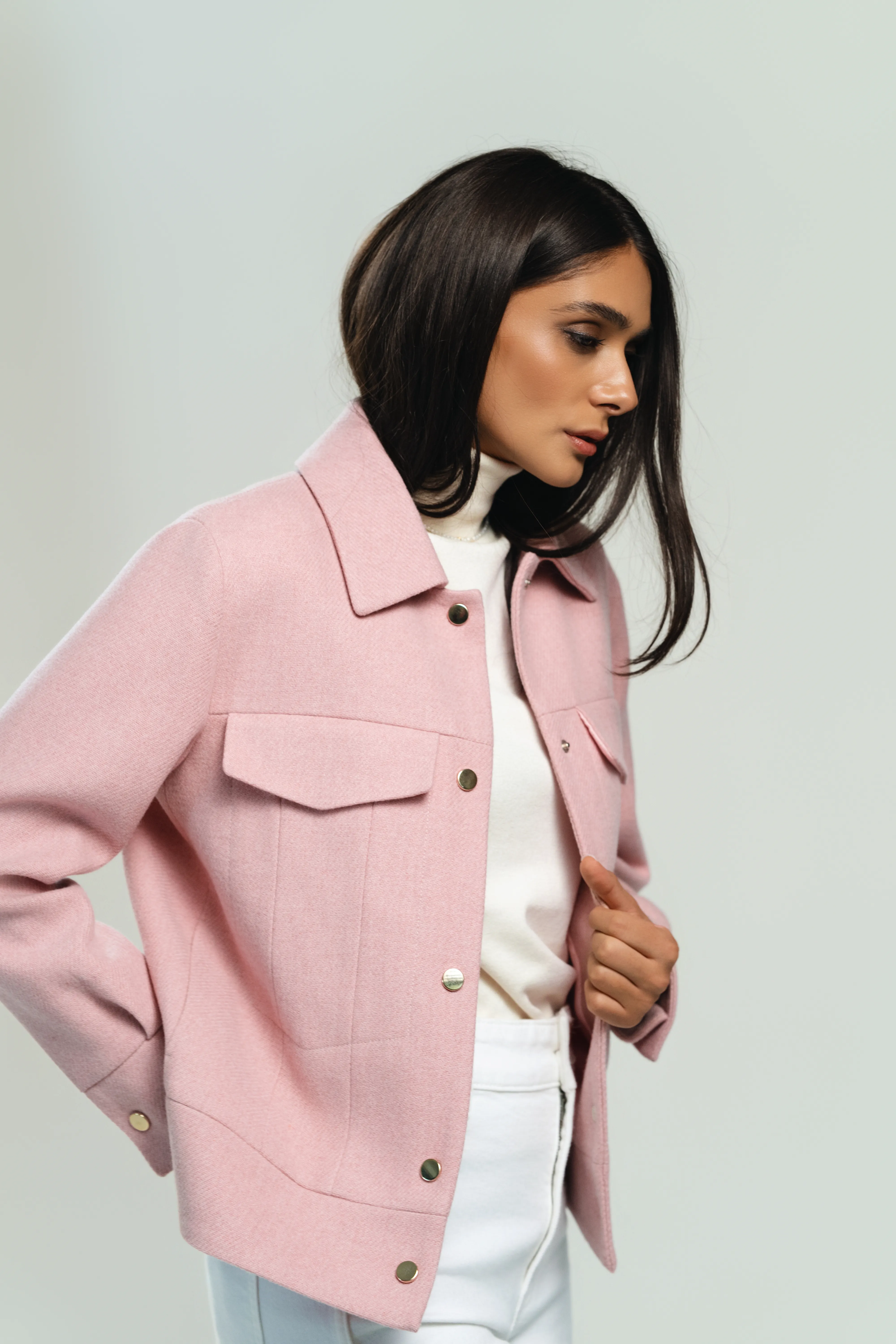 A woman in a soft pink jacket over a white turtleneck glances down, close three-quarter crop